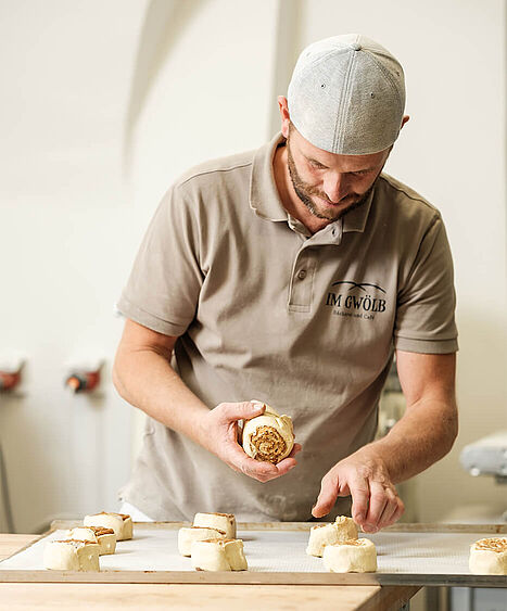Ein Bäcker mit Kappe backt eine Nussschnecke in der Bäckerei in Vorchdorf