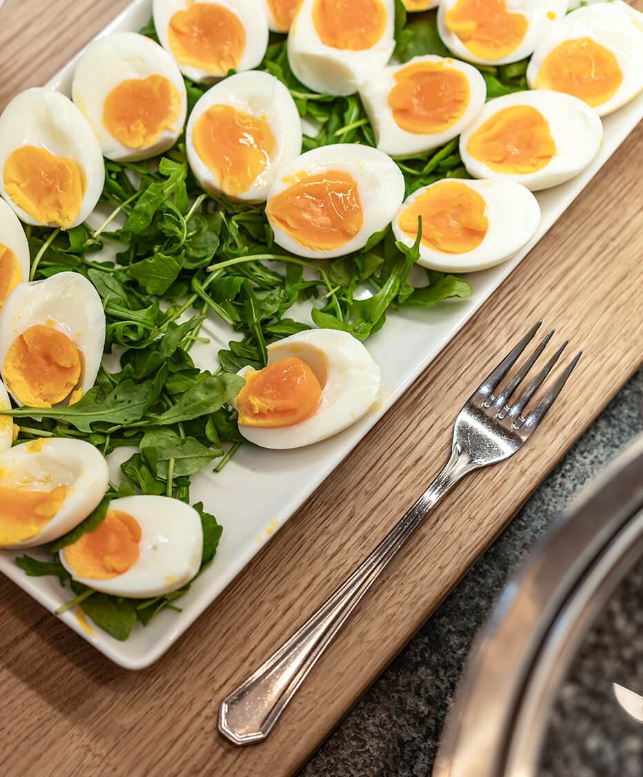 Frischgekochte Eier, halb aufgeschnitten und präsentiert mit rucola auf weißem eckigem Teller im Hotel Krone in Mondsee