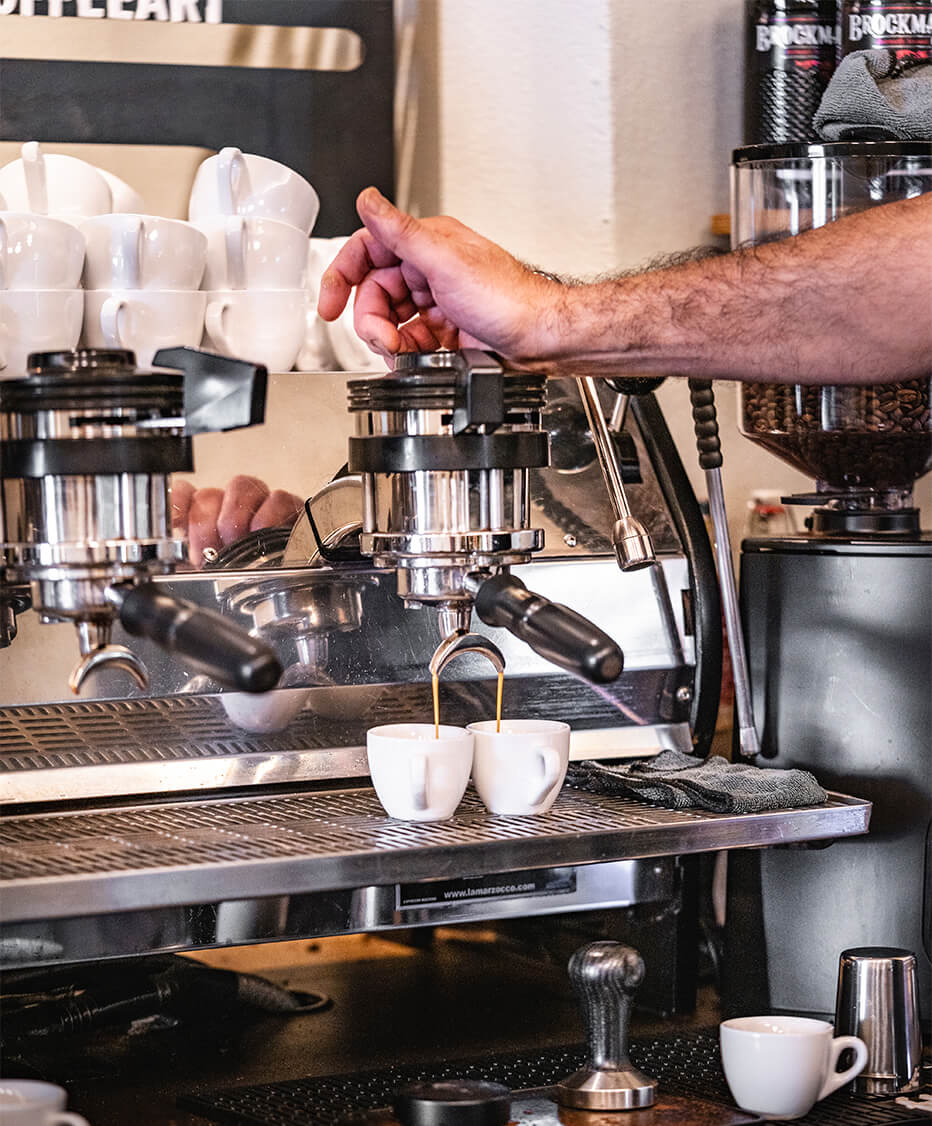 Siebträger-Kaffeemaschine im Betrieb, zwei Tassen frischer Espresso von Barista Tarkan zubereitet