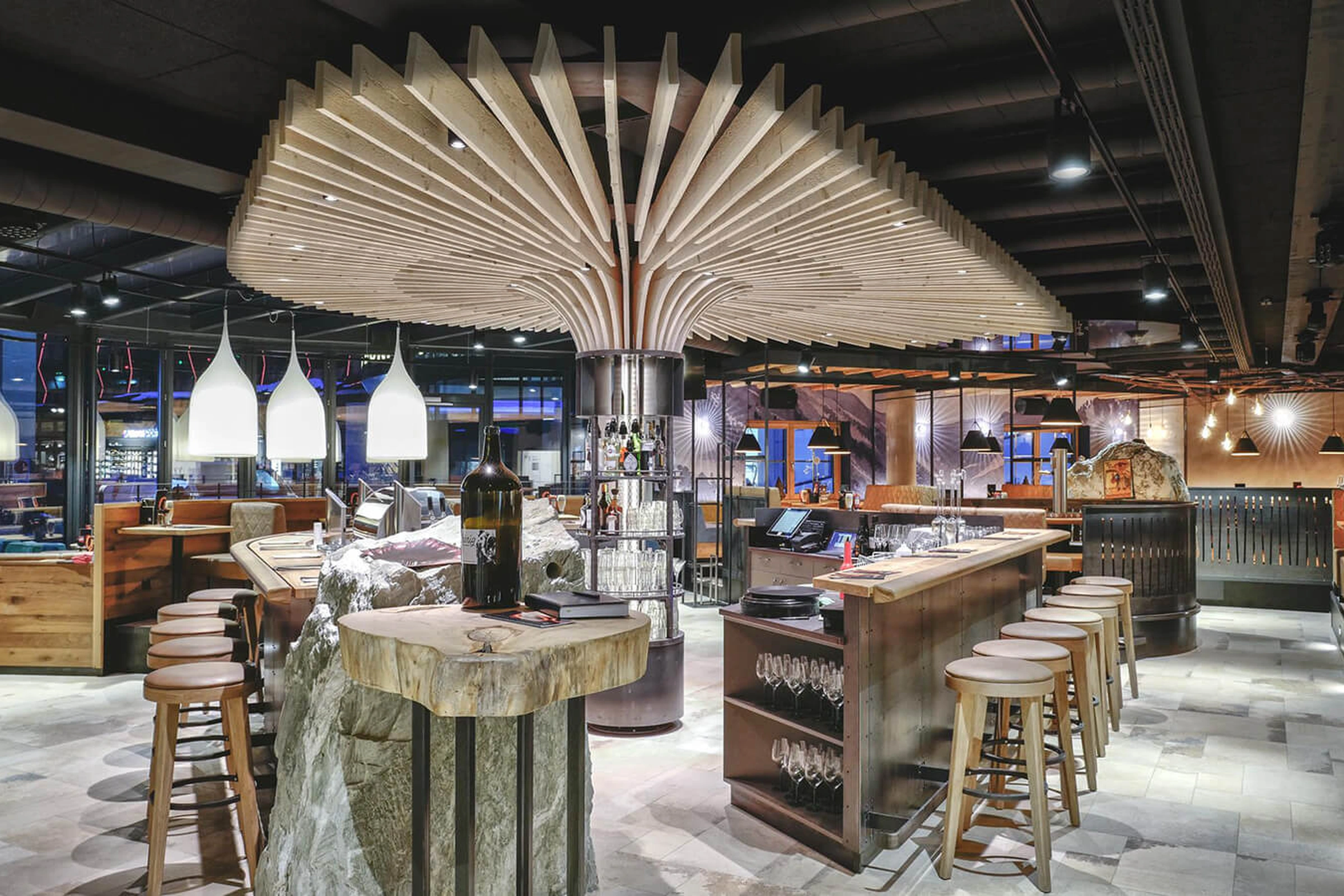 Beeindruckender Barbereich des Restaurants Gaspis in Gerlos mit fächerförmiger Holzskulptur an der Decke, Steintisch auf Felsensockel und rustikaler Holztheke.