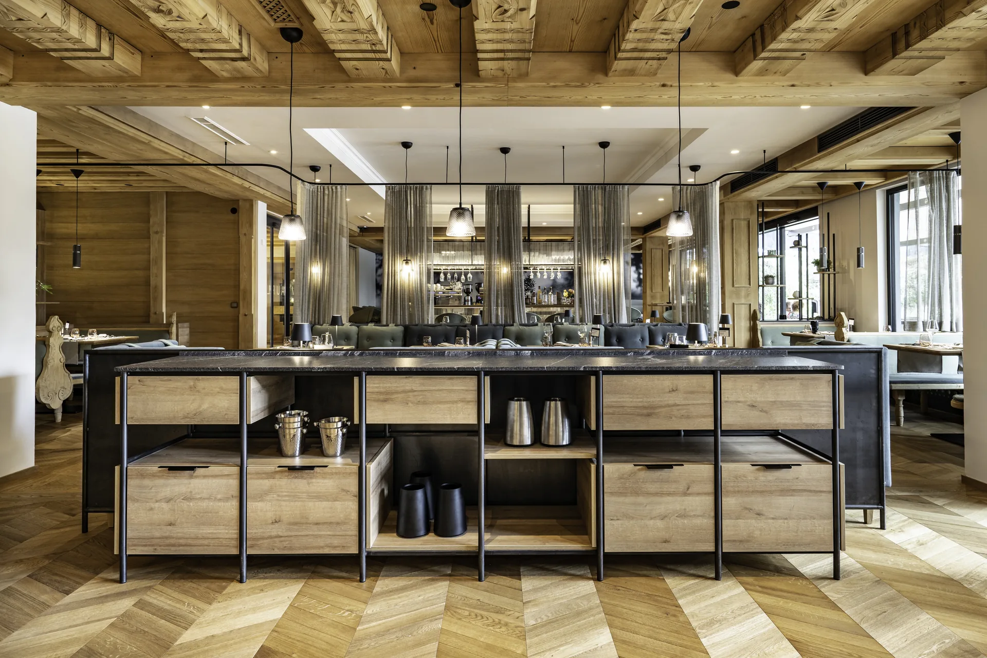 Gastraum im Pirchnerhof Reith mit zentralem Serviertisch in Marmor und Holz, Pendelleuchten, grauer Sitzbank, Bar im Hintergrund und Fischgrätparkett.