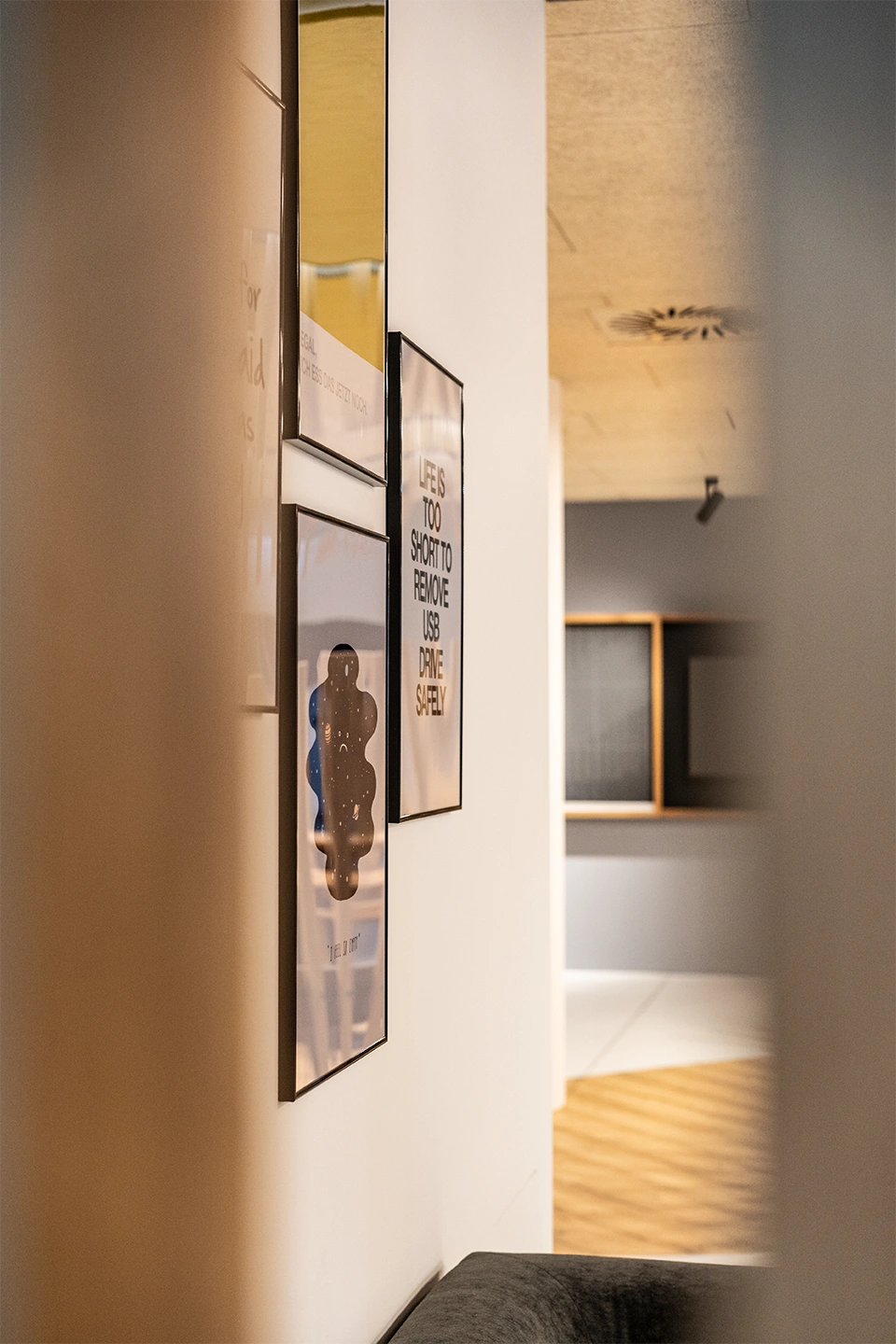 Galeriewand mit gerahmten Kunstdrucken und humorvollen Zitat-Postern, im Hintergrund der Übergang zum Holzstab-gestalteten Speisesaalbereich.