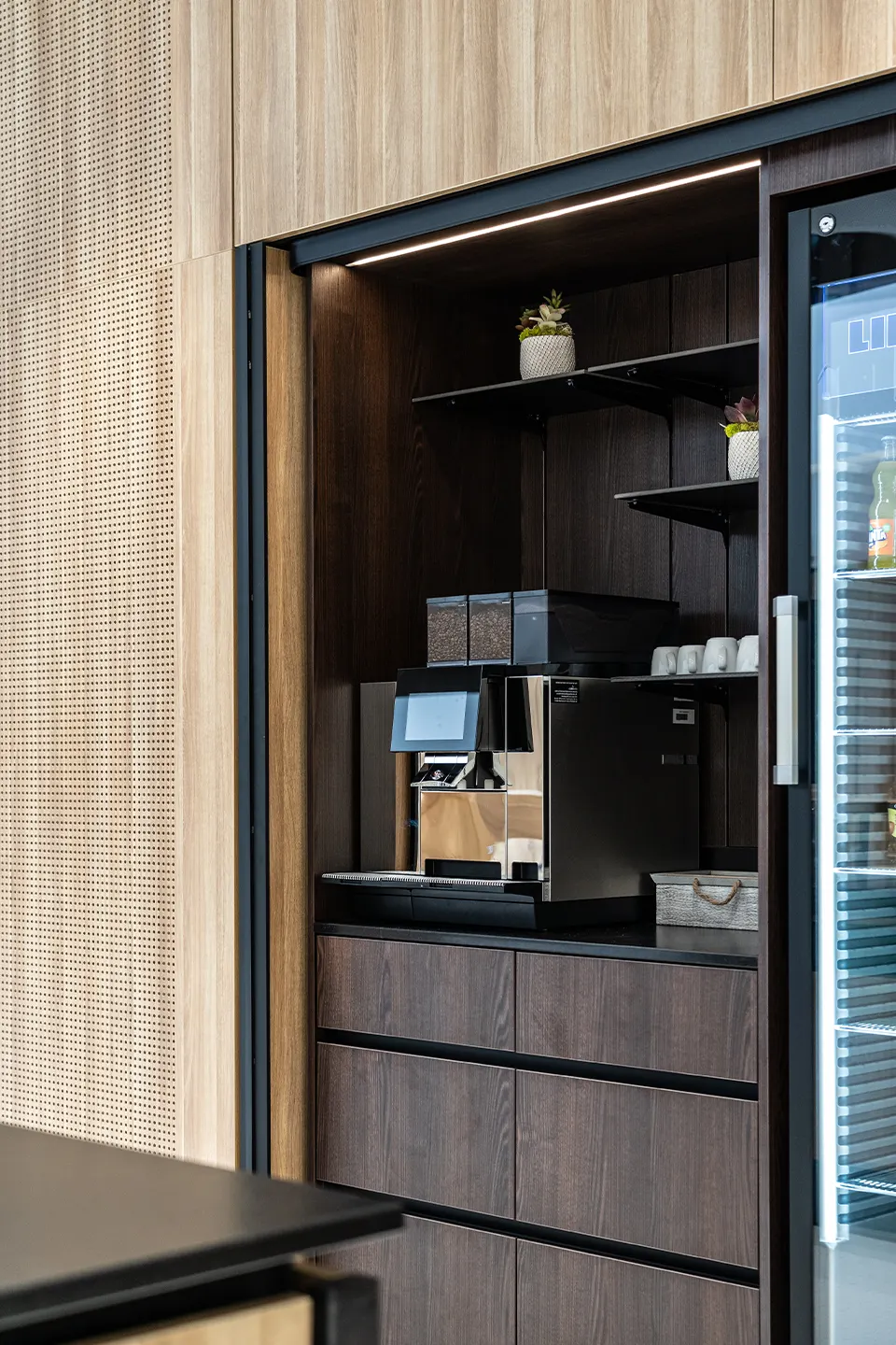 Kaffee-Bar im BR Forum Eggelsberg mit integriertem Kaffeevollautomaten, Holzschrank mit Schiebetür, Regalböden mit Sukkulenten und Kühlschrank