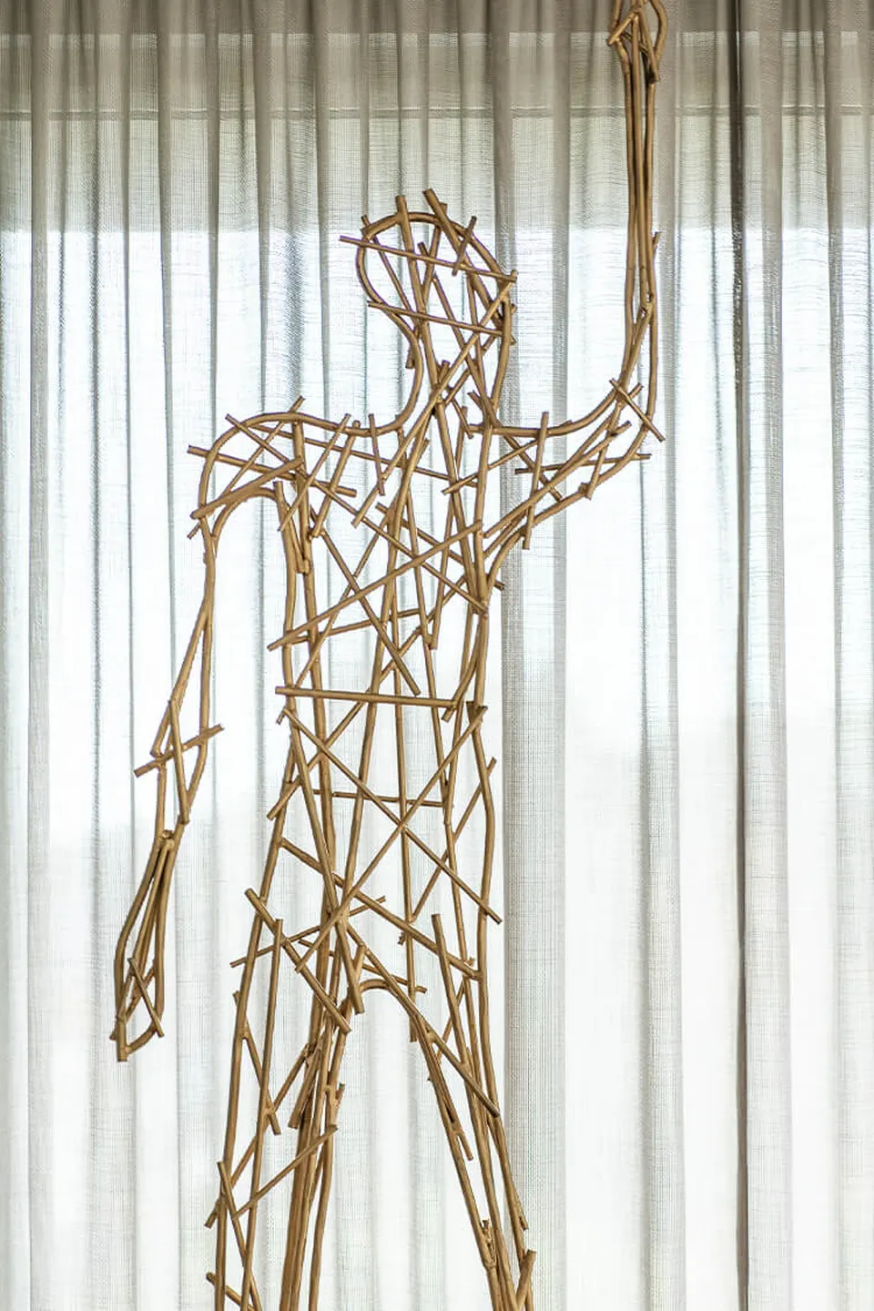 Großformatige Skulptur einer menschlichen Figur aus verschlungenen Rattanstäben vor einem hellen Vorhang in der Biogena Healthworld in Koppl – ein ausgestreckter Arm greift nach oben.