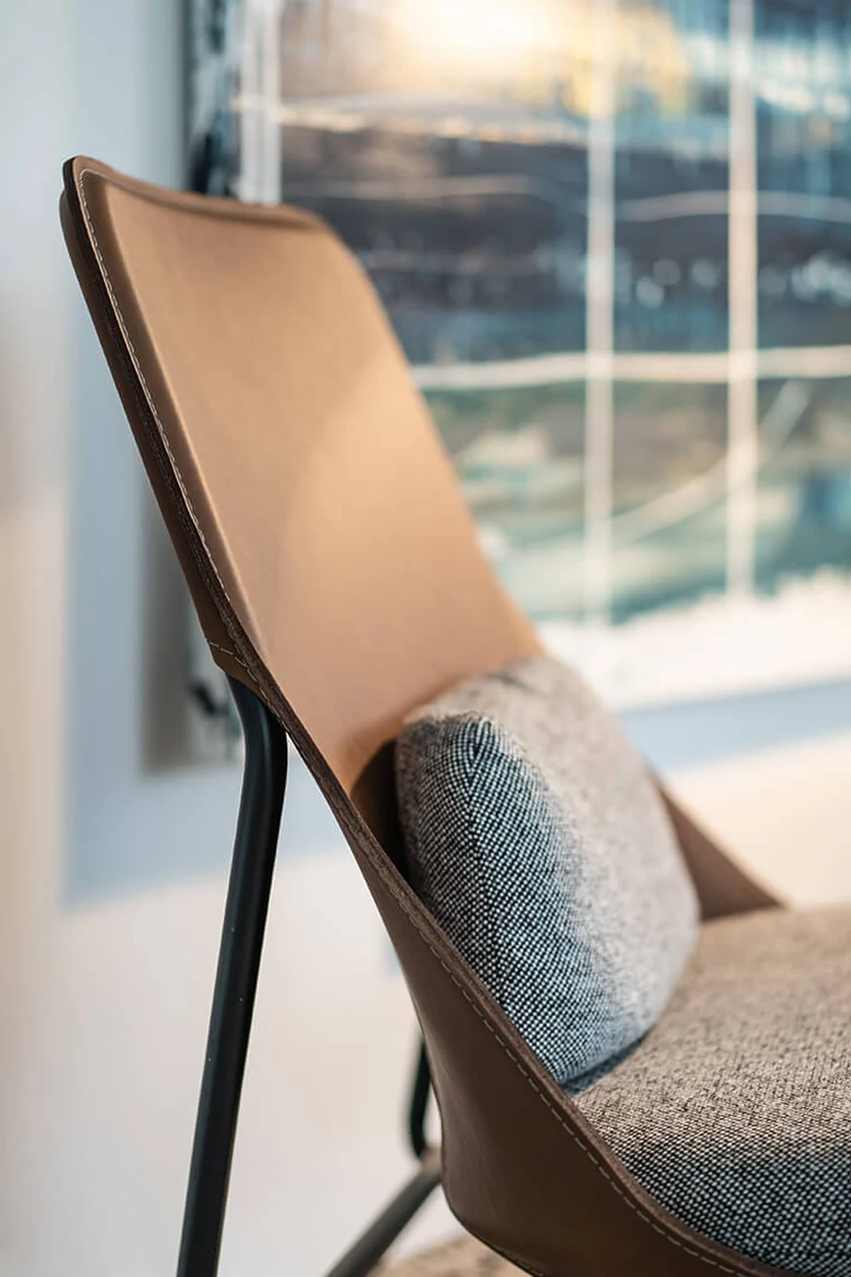 Detailaufnahme eines Designstuhls mit cognacfarbenem Lederrücken und grauem Stoffsitz auf schwarzem Metallgestell in der Biogena Healthworld in Koppl.