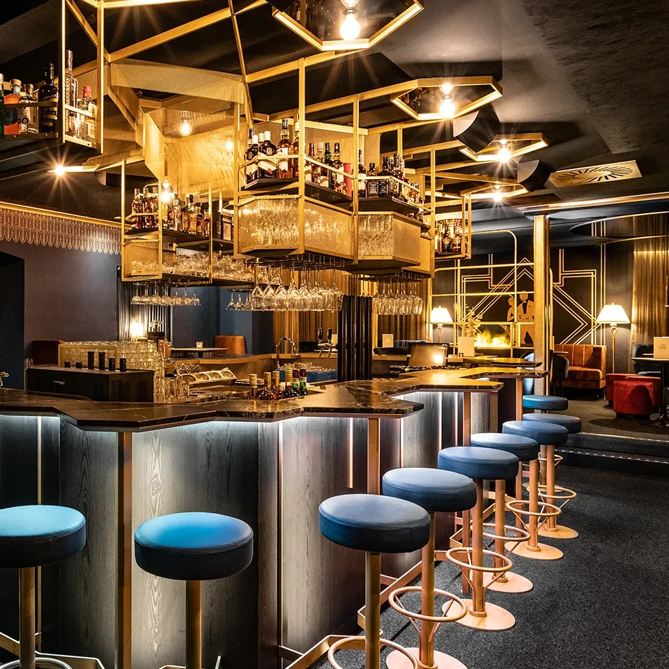 Exklusive Bar im Twenties-Stil mit goldenen Details, Design-Barhockern und hochwertigem Innenausbau