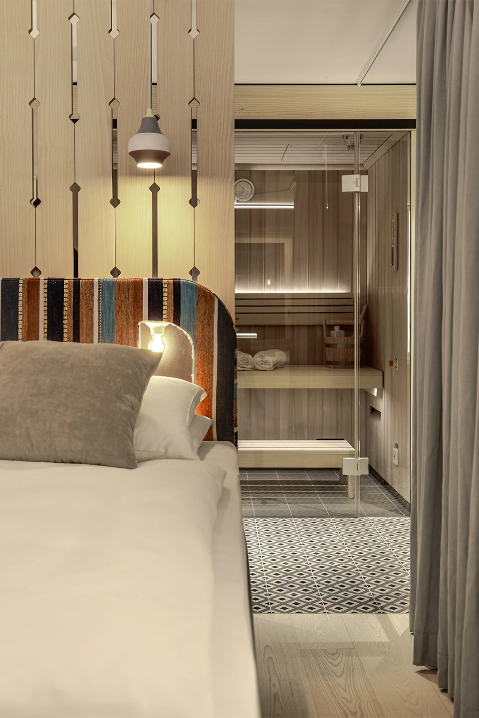 Blick vom Bett mit gemustertem Kopfteil auf eine integrierte Glassauna und dekorative Holzpaneele