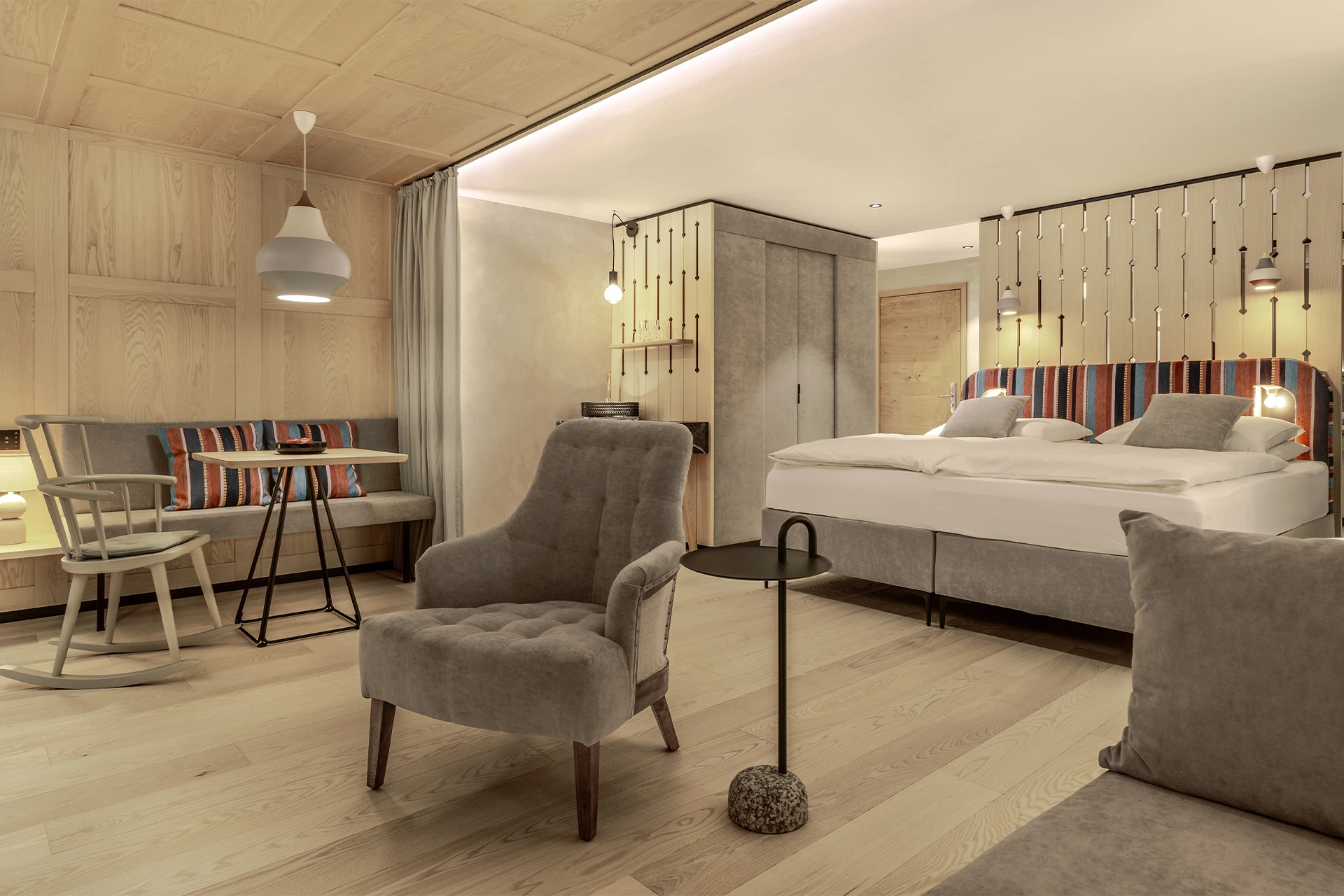Großzügiges Hotelzimmer in hellem Holzdesign mit Doppelbett, gemütlichem Sessel und einer integrierten Sitzecke