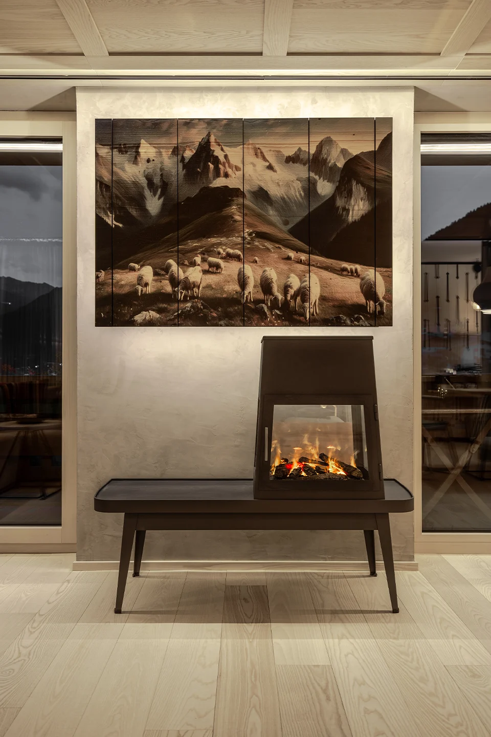 Fokus auf einen modernen, schwarzen Design-Kamin unter einem mehrteiligen Leinwandbild mit Alpenpanorama.