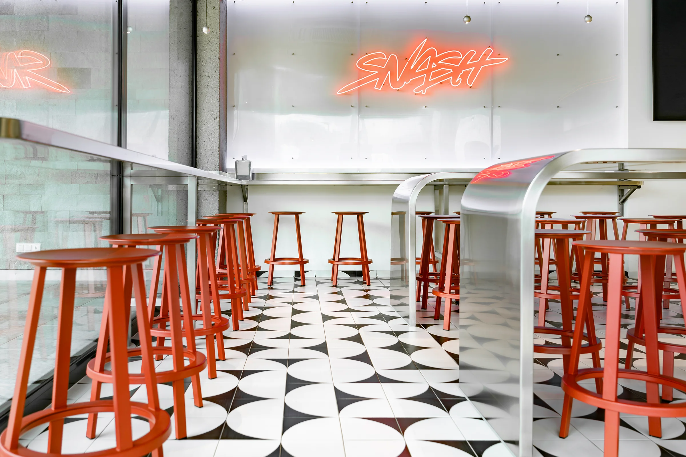 Modernes SB Restaurant in Bürs mit klarer Innenarchitektur, grafischem Fliesenboden, roten Barhockern und offenem Raumkonzept
