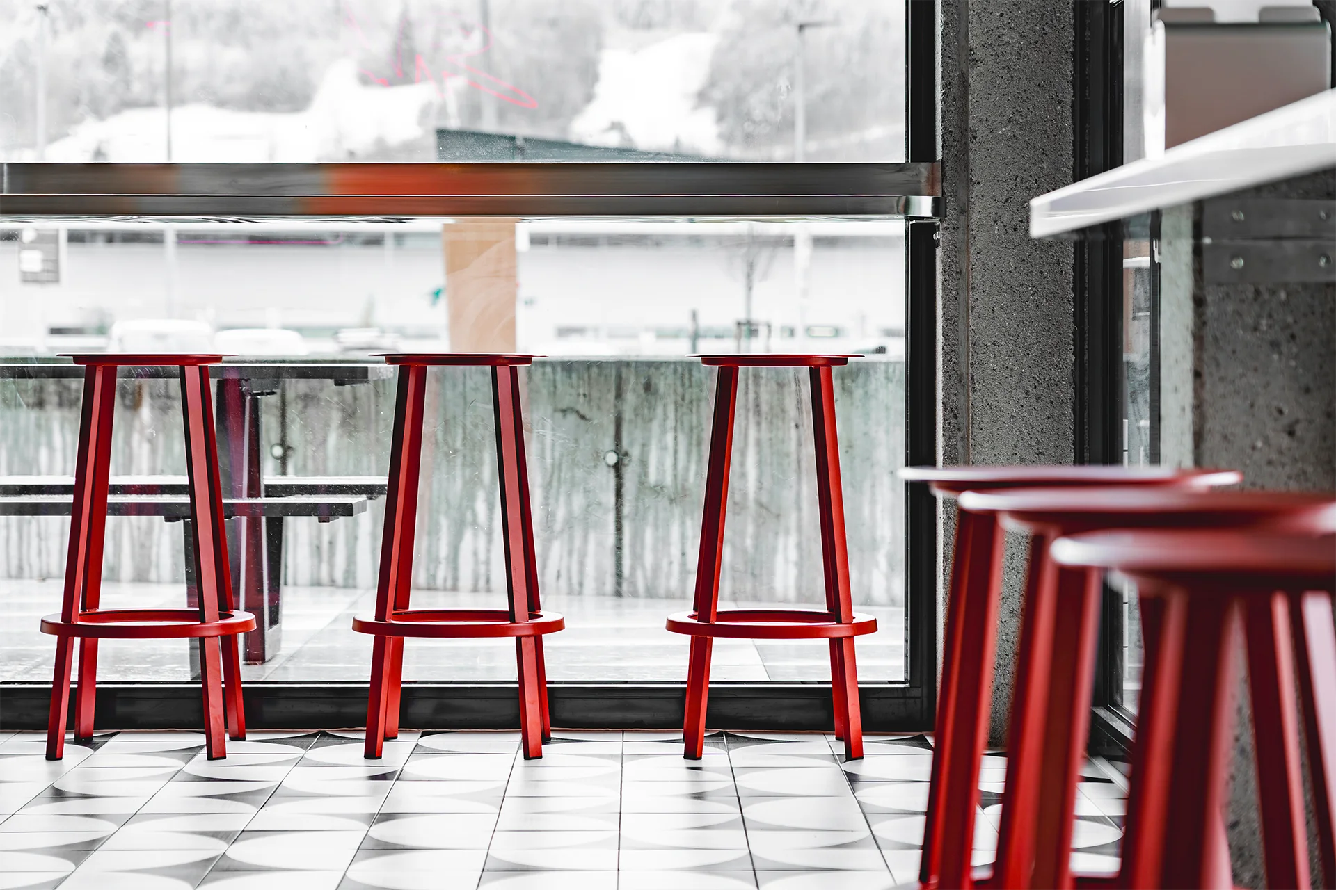Hochbereich mit roten Hockern am Fenster als kompakte Sitzlösung im Selbstbedienungsrestaurant