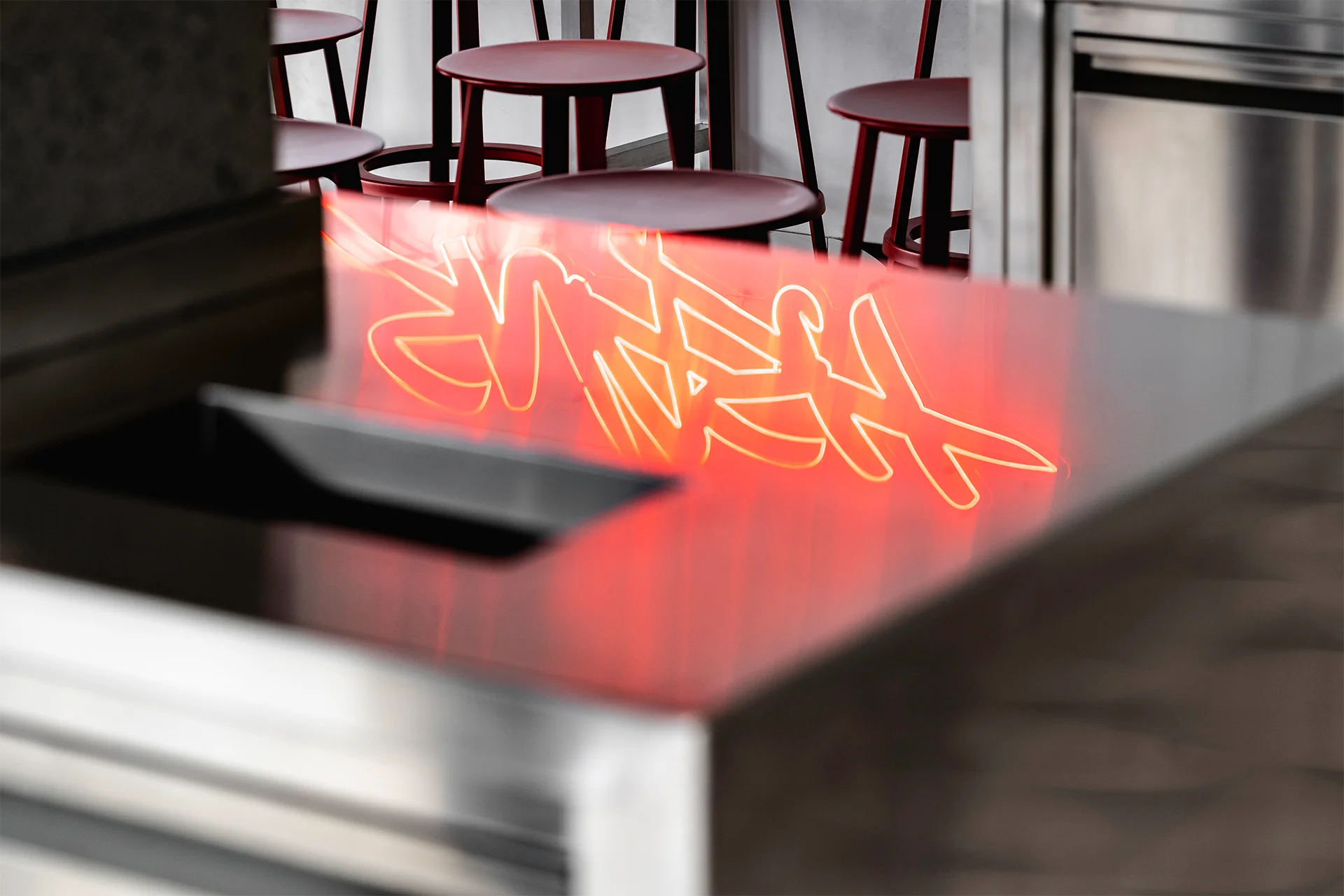 Neonlogo mit Spiegelung auf Edelstahloberflächen als prägnantes Designelement im Burger Restaurant