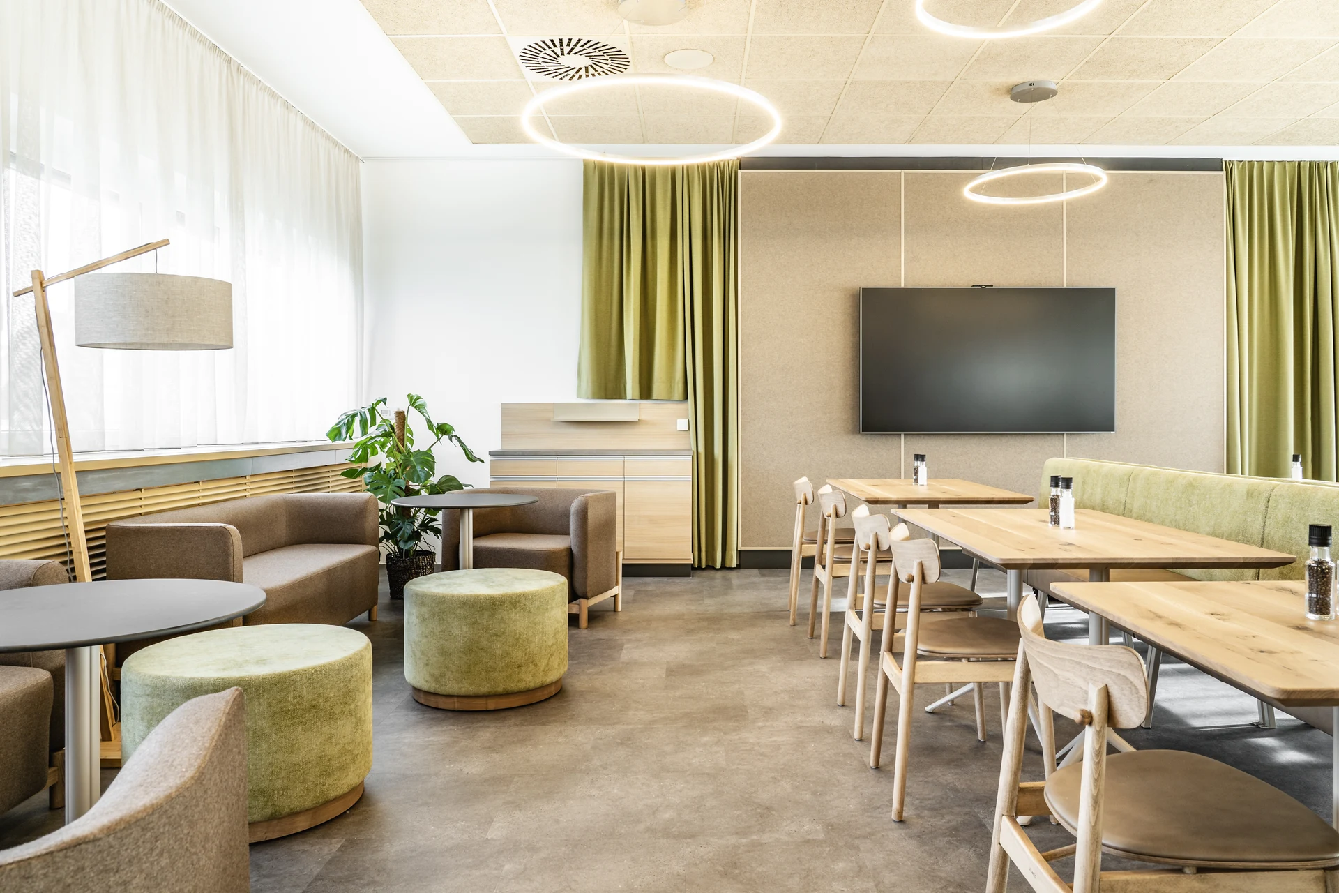 Lounge- und Seminarraum des Spitzeria Attnang mit braunen Sesseln, grünen Poufs, Holztischen, TV und grünen Vorhängen.