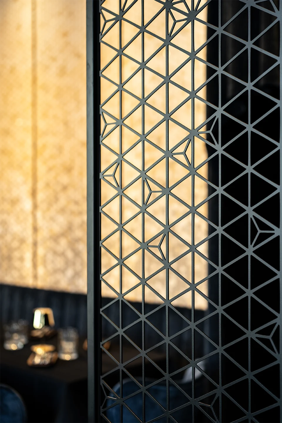 Detailaufnahme eines geometrischen Metall-Raumteilers mit japanischem Sashiko-Muster vor einer hinterleuchteten Goldwand.