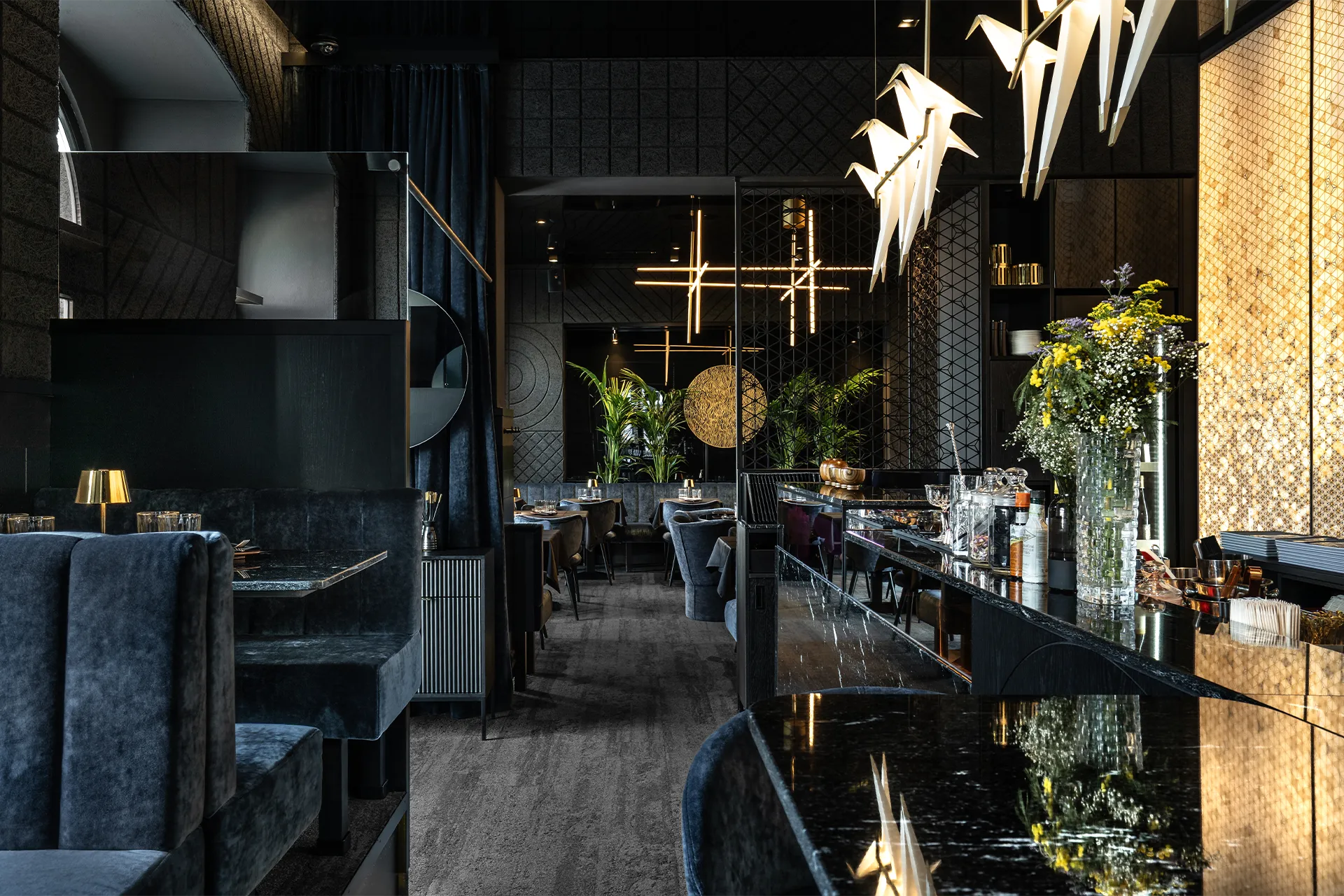 Blick vom Eingangsbereich mit schwarzem Marmortresen und Origami-Kranich-Leuchten in den eleganten Hauptsaal des Restaurants.