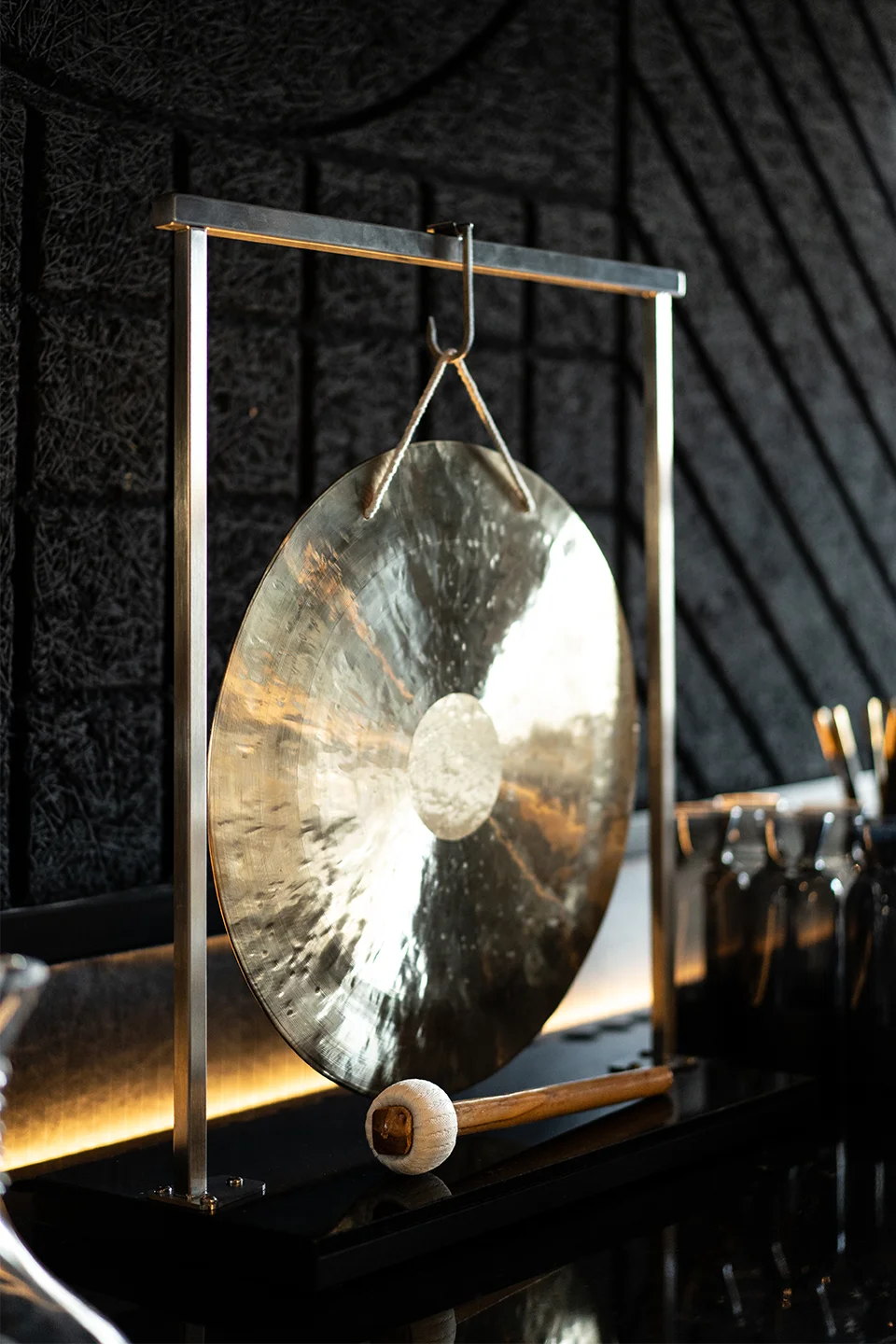Goldener Gong auf einem Metallständer vor einer strukturierten schwarzen Akustikwand als dekoratives Element im Restaurant.