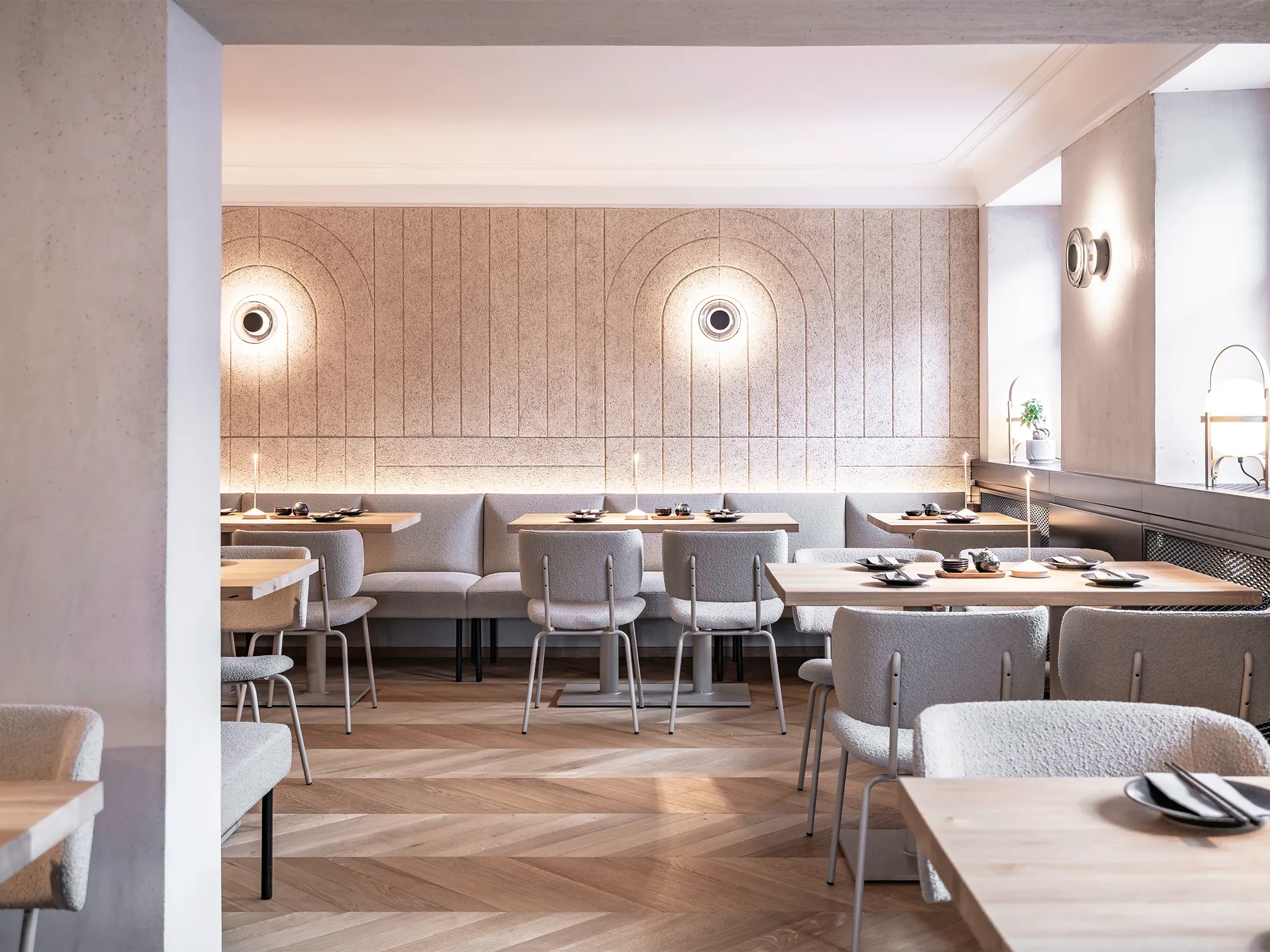 Gastraum im Sushi-Restaurant Hanako in Dornbirn mit gefrästen Heradesign-Akustikpaneelen, runden Wandleuchten und gepolsterten Sitzbänken.