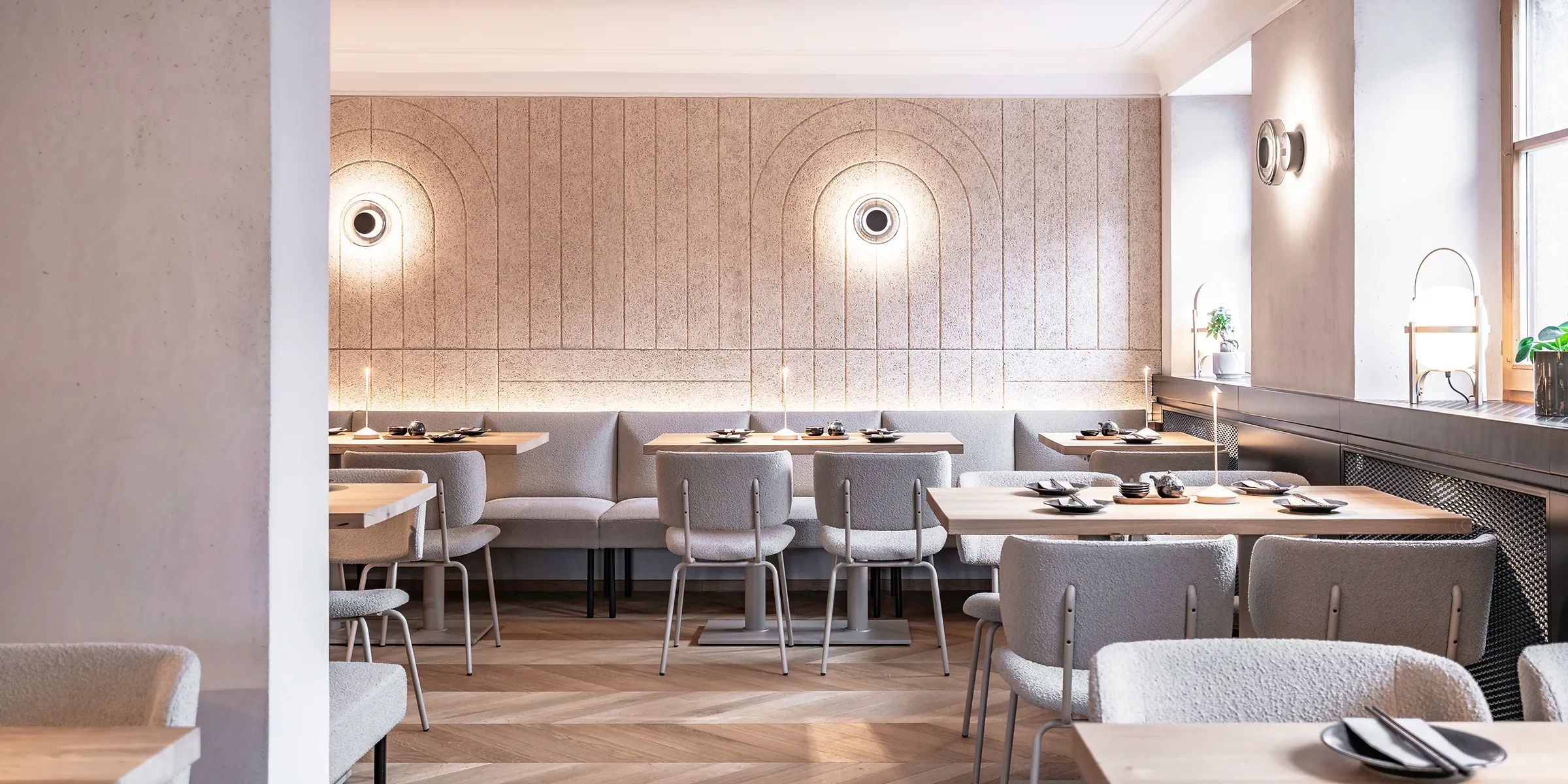 Gastraum im Sushi-Restaurant Hanako in Dornbirn mit gefrästen Heradesign-Akustikpaneelen, runden Wandleuchten und gepolsterten Sitzbänken.