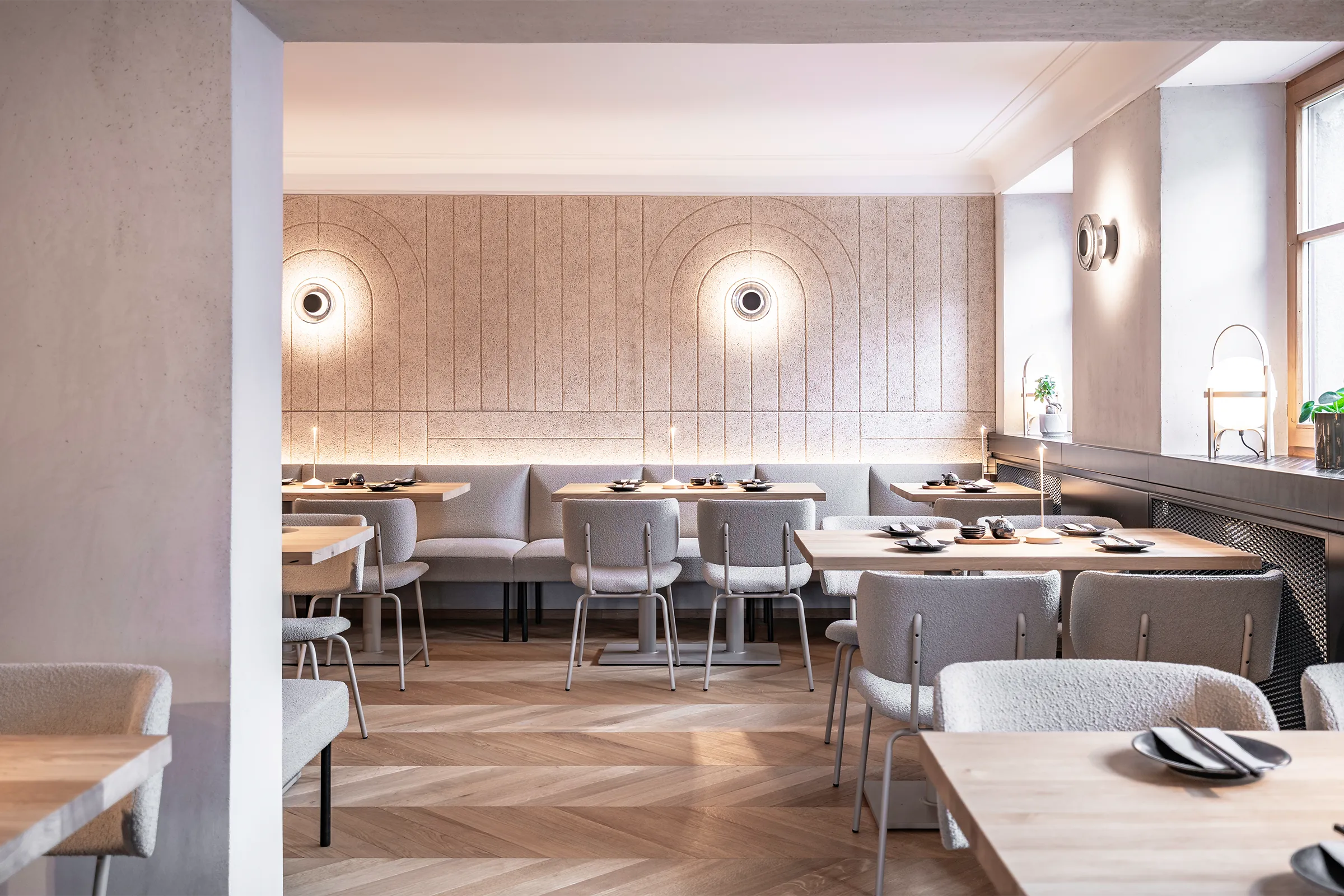 Gastraum im Sushi-Restaurant Hanako in Dornbirn mit gefrästen Heradesign-Akustikpaneelen, runden Wandleuchten und gepolsterten Sitzbänken.