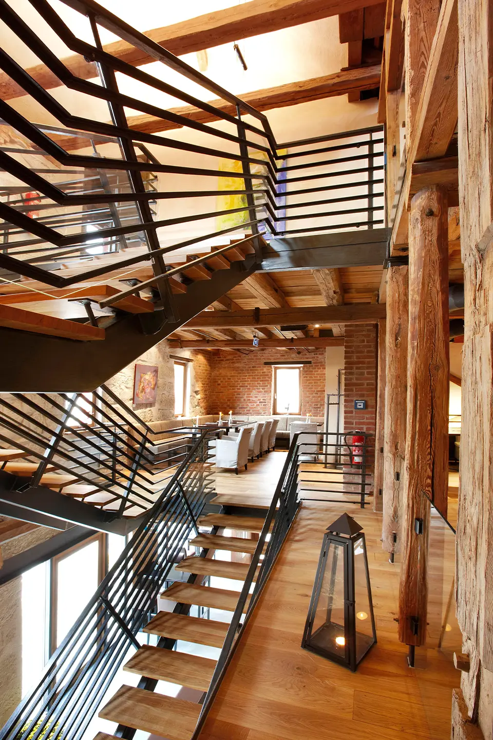 Mehrstöckige Industrietreppe aus Stahl und Holz verbindet die Etagen des Restaurants, gerahmt von massiven historischen Holzbalken und einer Backsteinwand.
