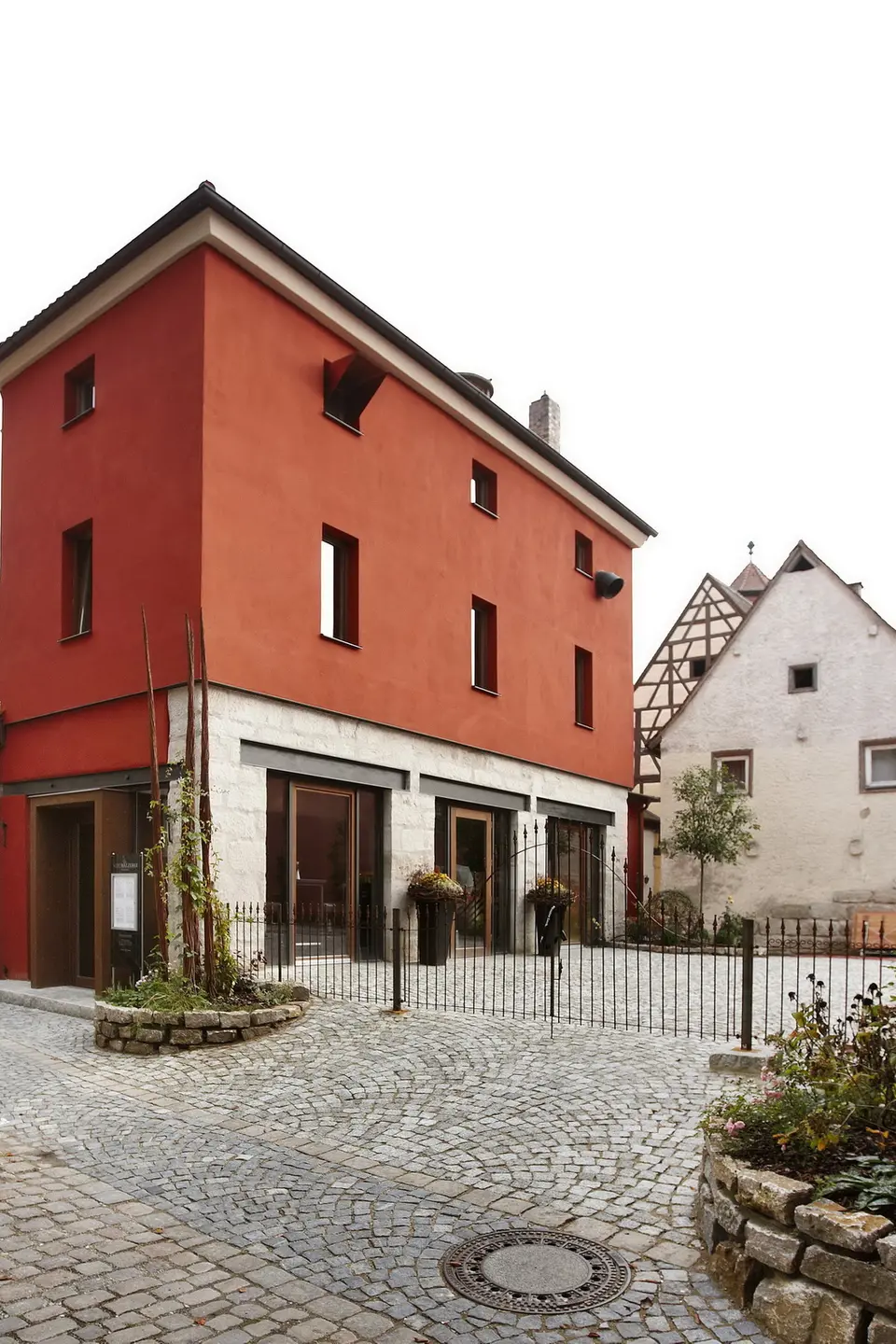 Außenansicht des Restaurants in einem terrakottaroten Altstadtgebäude mit Natursteinsockel, modernen Panoramafenstern und historischem Kopfsteinpflaster im Vordergrund.