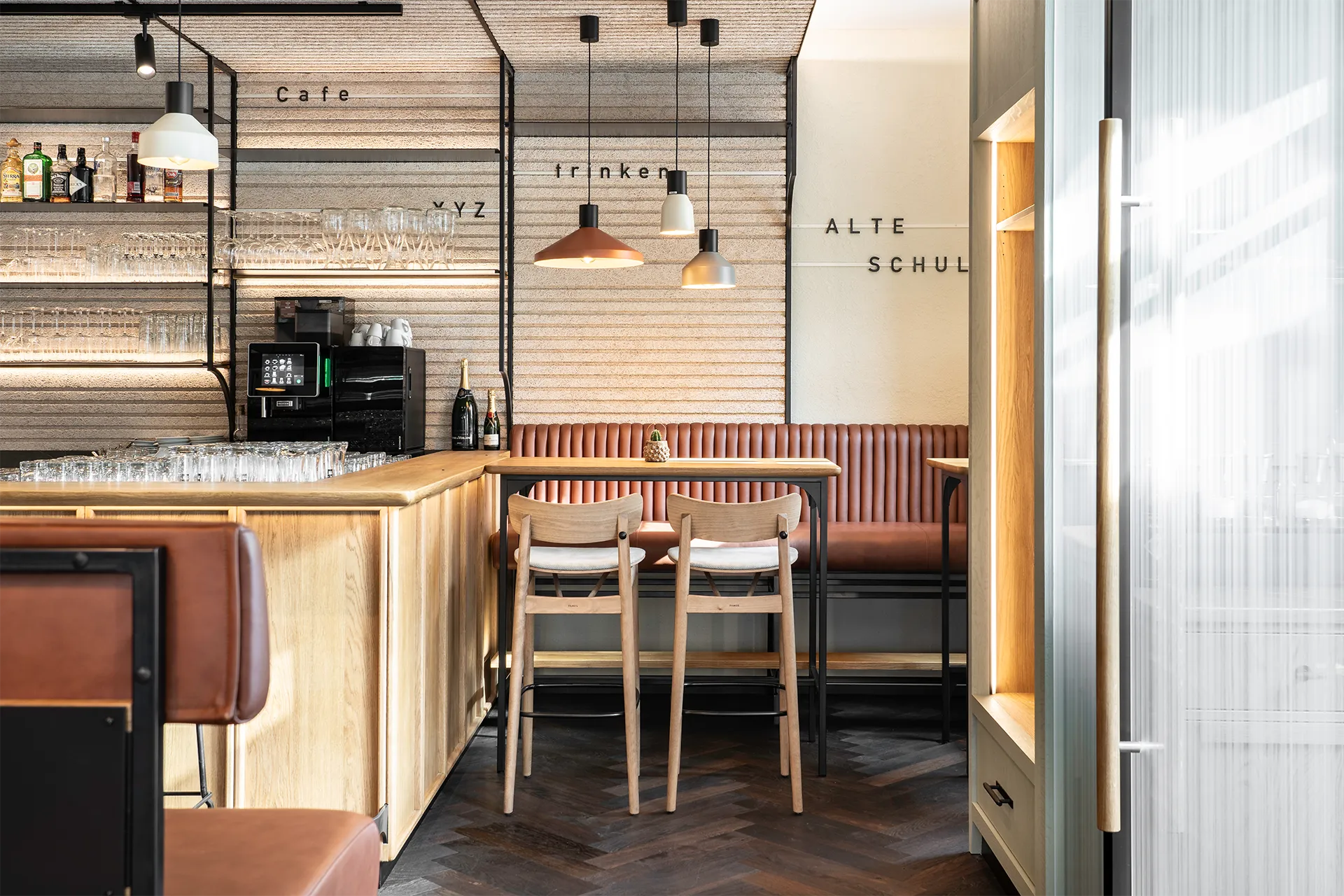 Blick auf einen Teil der Bar und eine gepolsterte Sitzbank vor einer Wand mit den Schriftzügen „Cafe“, „trinken“ und „ALTE SCHULE“.