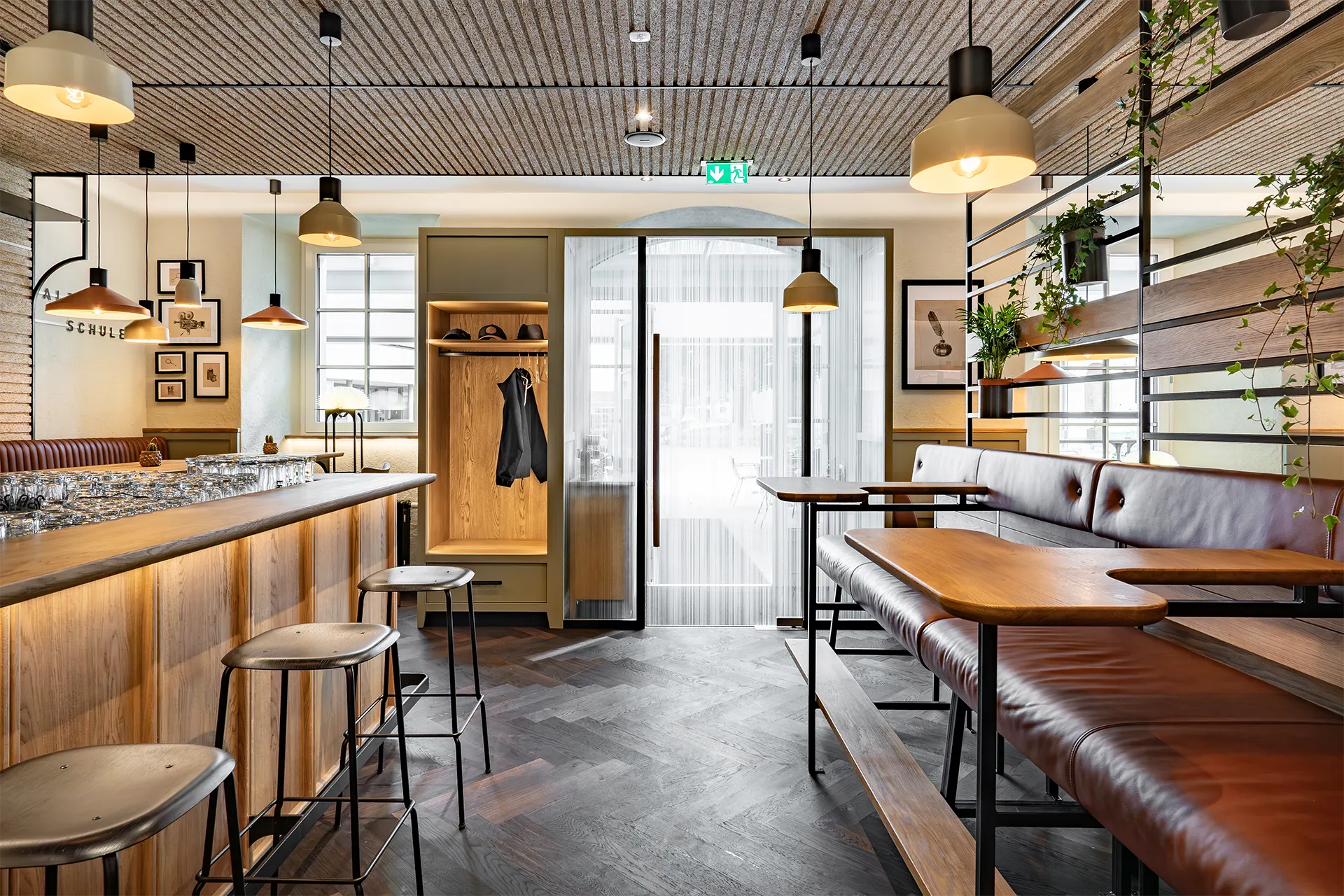 Der Eingangsbereich des Cafés mit einer hölzernen Garderobe, gemütlichen Lederbänken und Blick durch die Glastür nach draußen.