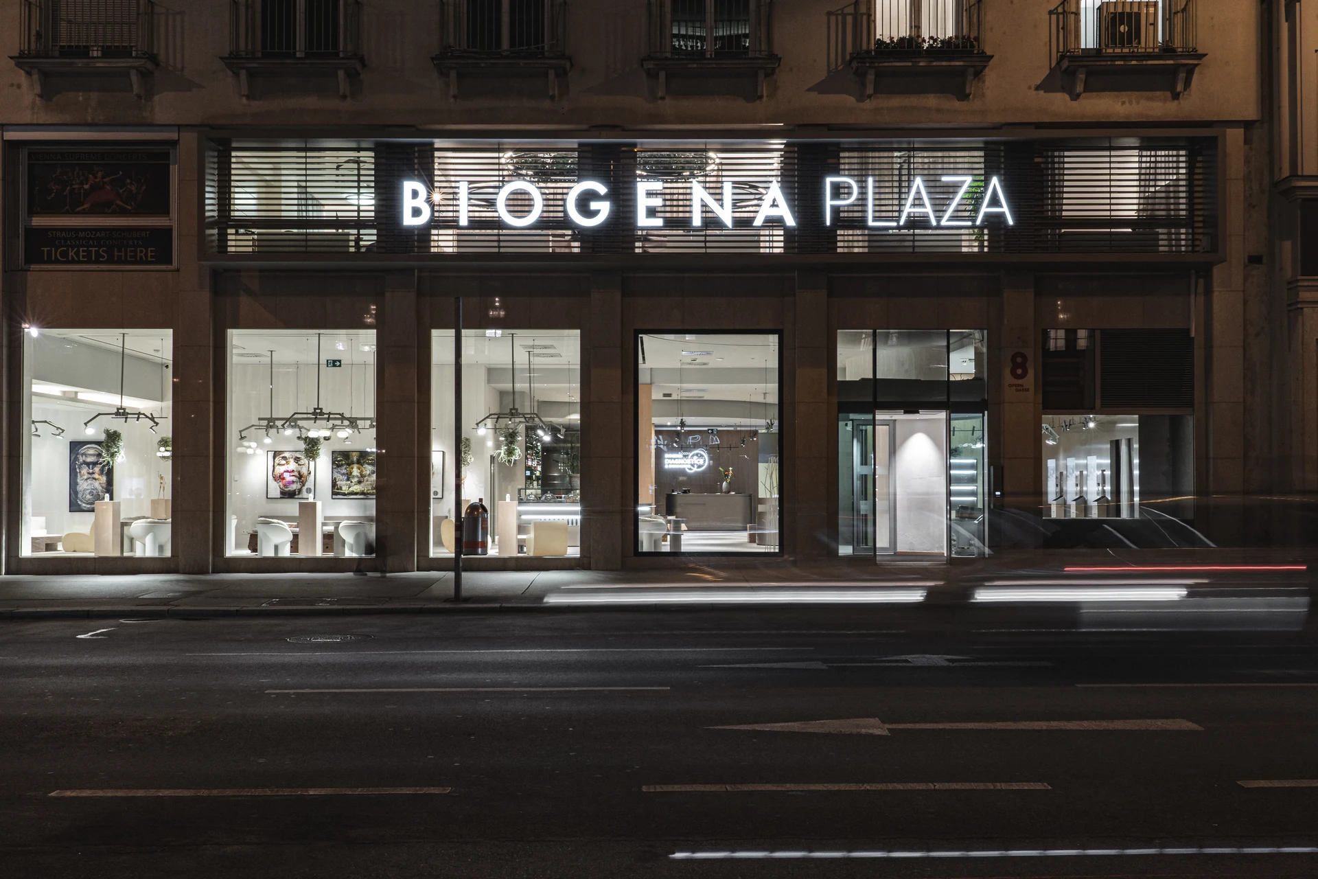 Nächtliche Außenansicht der Biogena Plaza an der Operngasse Wien mit leuchtendem Schriftzug und Blick durch die Glasfront in den hell erleuchteten Innenraum