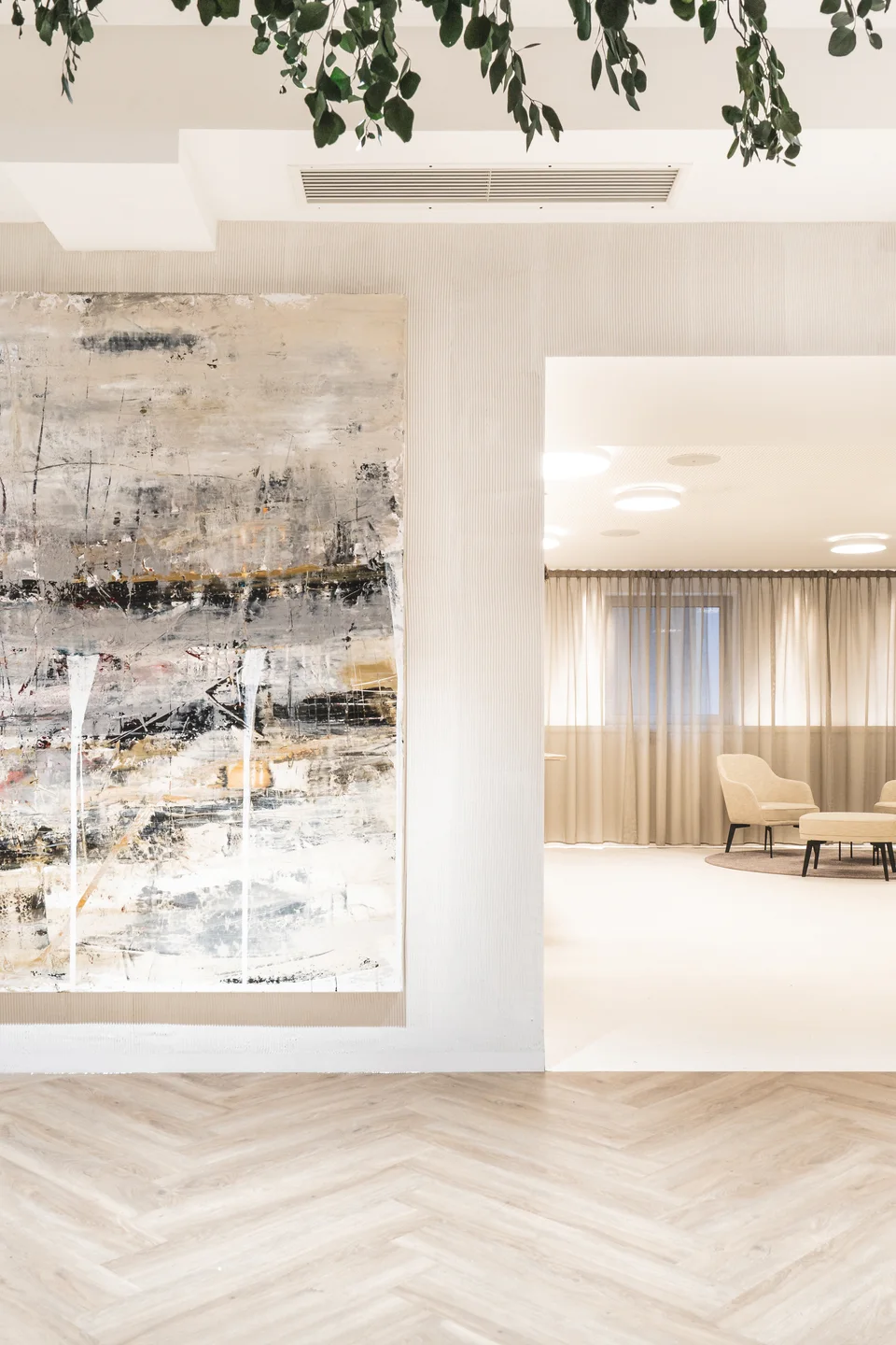Helles Interieur der Biogena Plaza Wien mit großformatigem abstraktem Gemälde, Fischgrätparkett und Blick in den Loungebereich mit beigen Sesseln