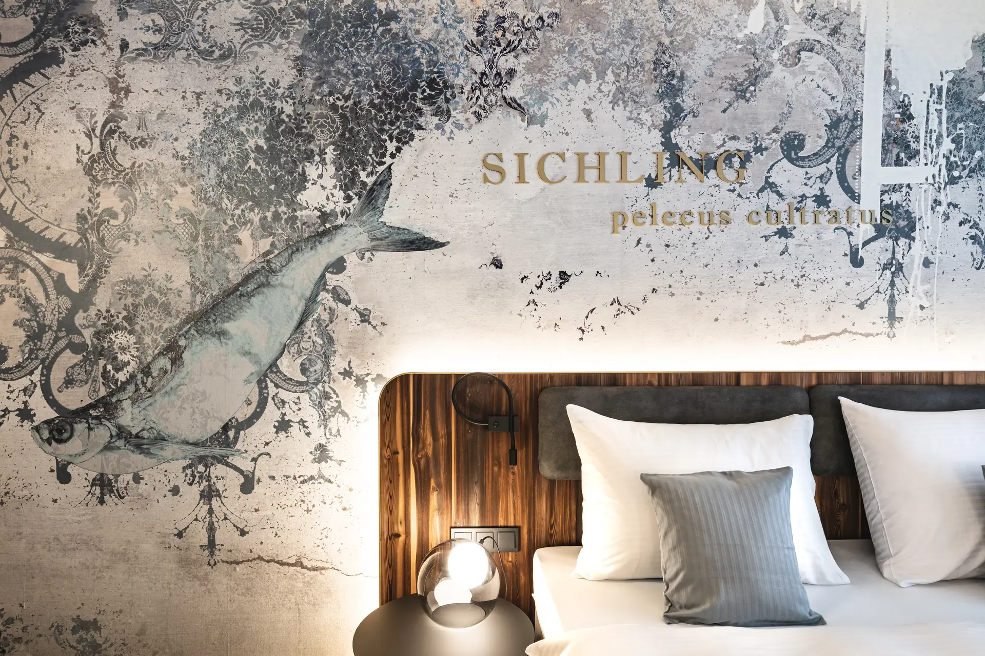 Detailansicht des Bettes im Hotel Blauer Bock Passau mit kunstvoller Wandtapete mit Fischmotiv und goldenem „Sichling