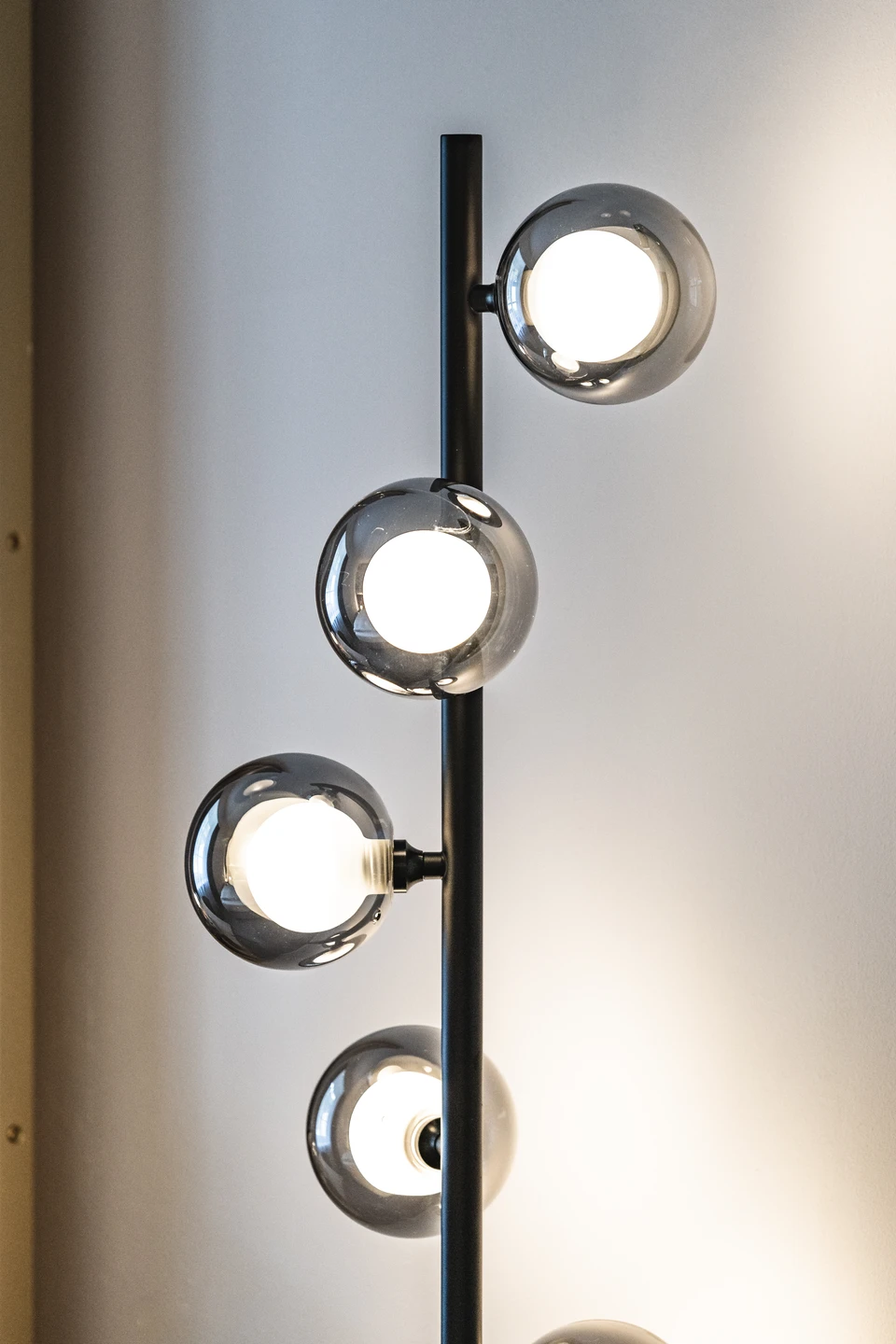 Detailaufnahme einer Stehlampe im Hotel Blauer Bock Passau mit schwarzem Metallstab und vier rauchgrauen Glaskugelleuchten vor hellem Wandhintergrund.