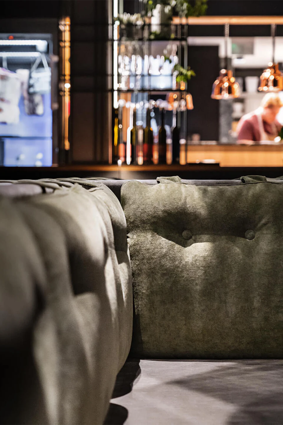 Der modern gestaltete Gastraum eines Fine-Dining-Restaurants mit kreuzförmig angeordneten, olivgrünen Sitzbänken und Tischen vor großen Panoramafenstern.