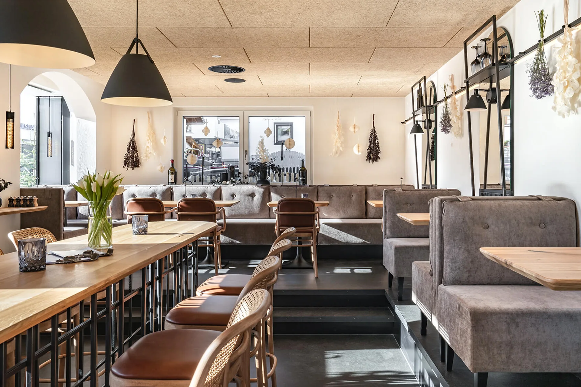 Ein erhöhter Sitzbereich im Bistro mit Hochsitzer aus Holz, Geflecht und Leder an einem Holztisch mit fein strukturierten Metalltischgestell.
