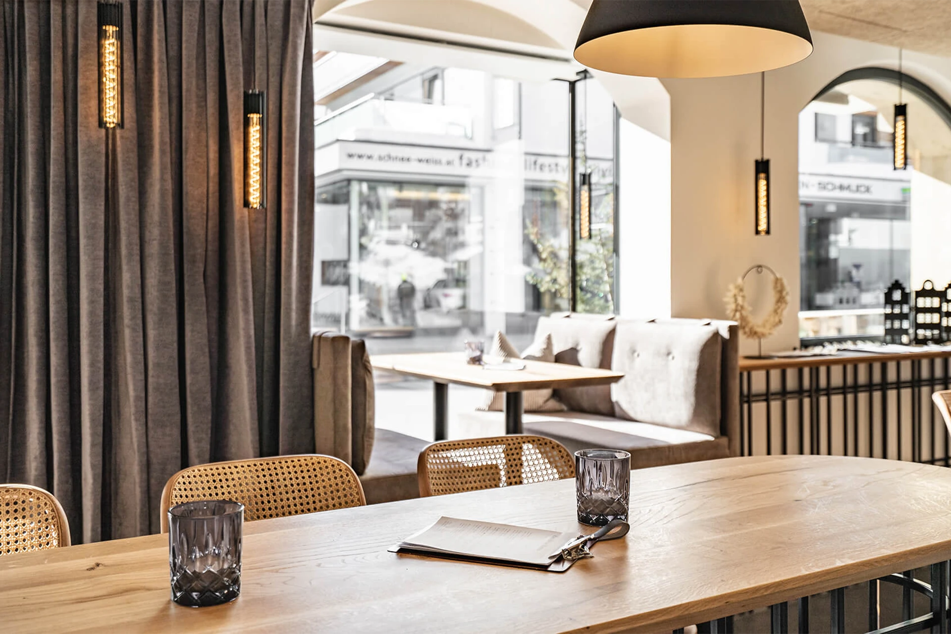 Ein erhöhter Sitzbereich im Bistro mit Hochsitzer aus Holz, Geflecht und Leder an einem Holztisch mit fein strukturierten Metalltischgestell.