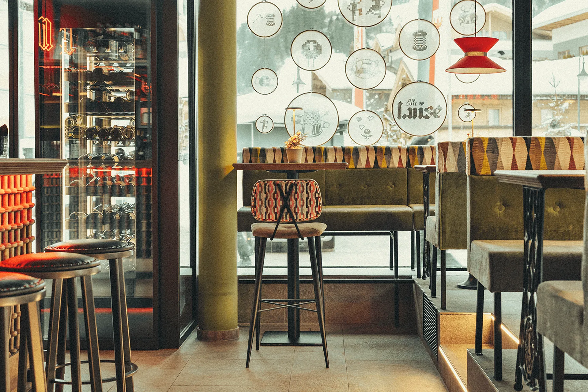 Ein erhöhter Sitzbereich mit bunt tapezierten Polsterbänken im Diner-Stil und einem großen, beleuchteten Weinklimaschrank im Hintergrund.