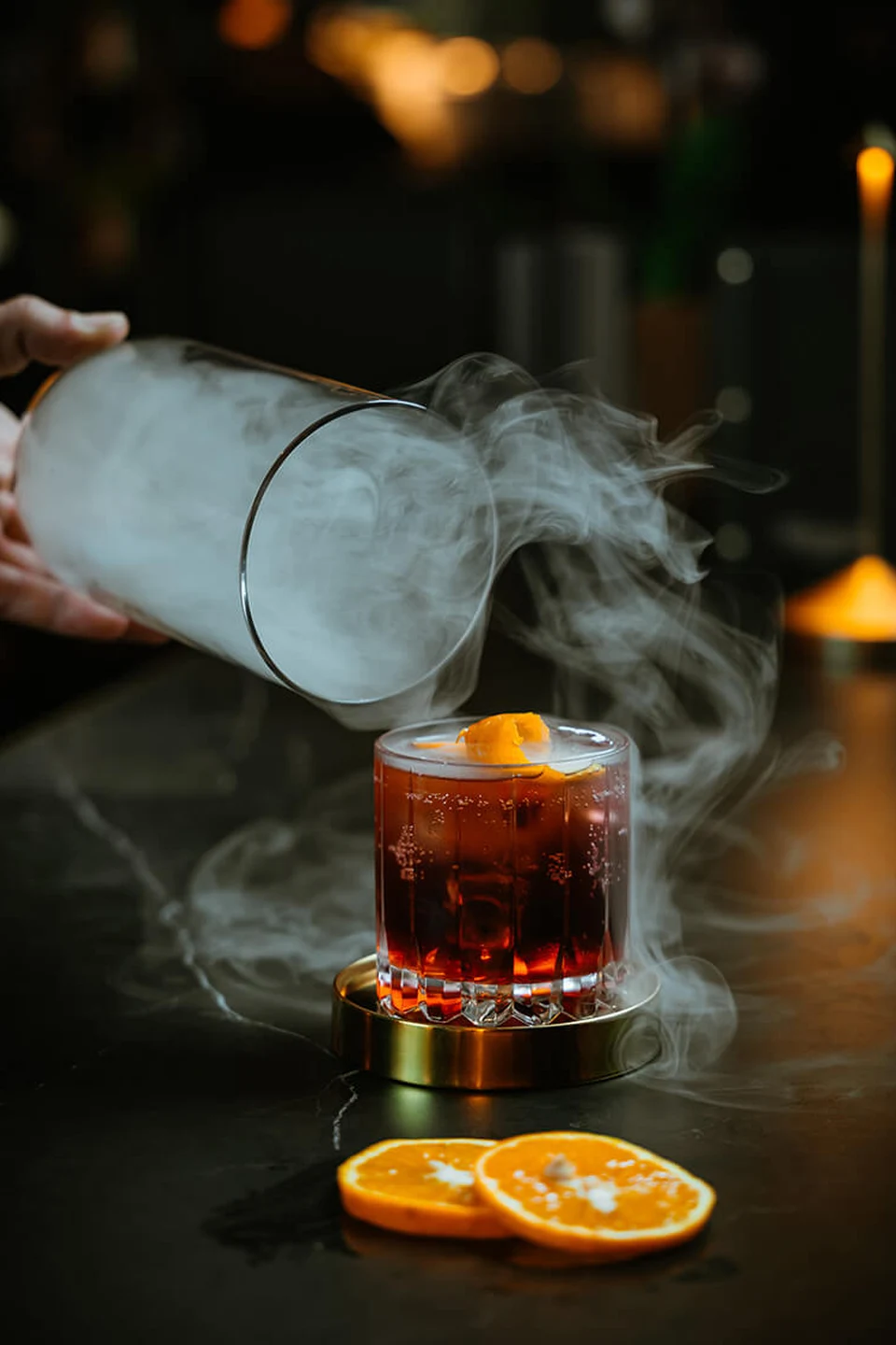 Barkeeper des Erbario in Schwaz bei der Zubereitung eines Signature-Cocktails mit Rauchglocke, Orangenzeste und goldenen Accessoires auf dem Marmortresen.