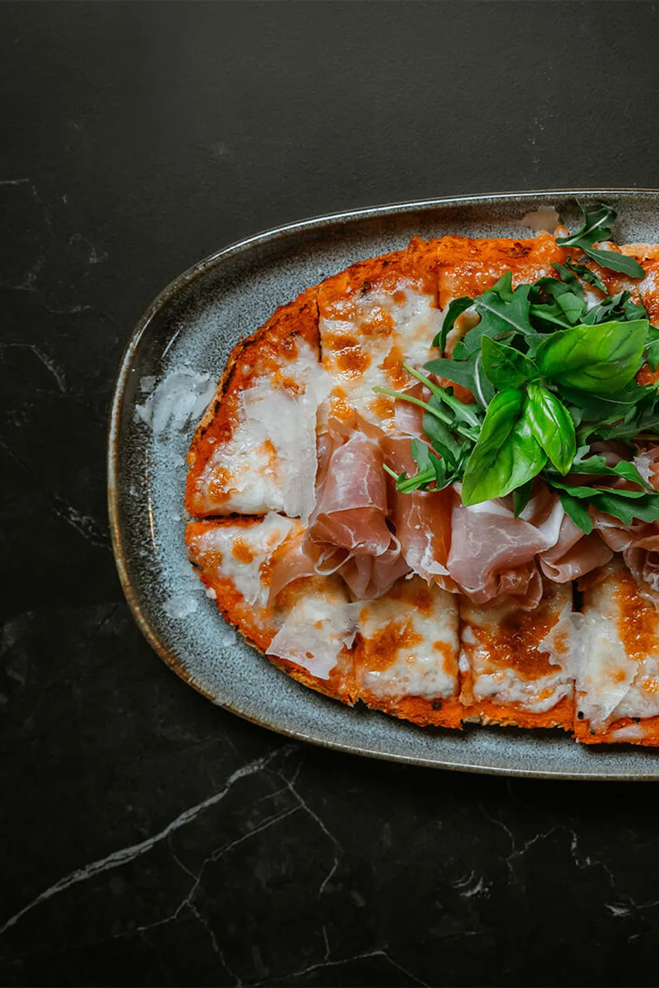 Hausgemachte Pizza mit Prosciutto, Mozzarella und Rucola auf einem rustikalen Keramikteller im Erbario in Schwaz.