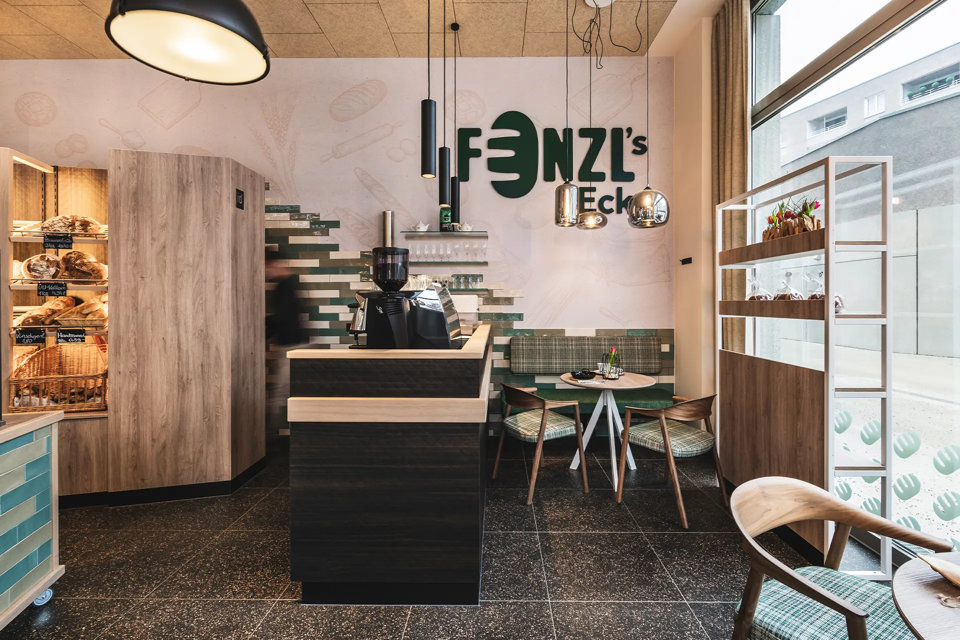 Blick auf den Kassenbereich mit dunkler Holztheke, Kaffeemaschine und türkis-grauen Wandfliesen unter dem grünen Fenzl's-Eck-Schriftzug