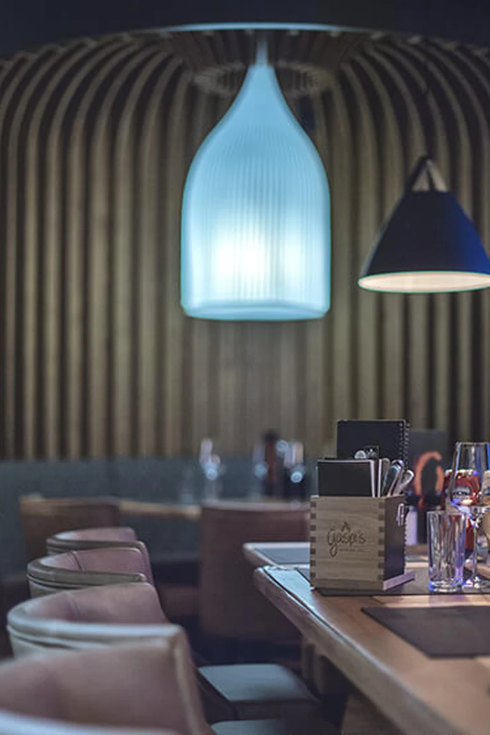 Stimmungsvoller Tischbereich im Restaurant Gaspis Gerlos mit blauer Hängelampe, gedecktem Tisch und gestalteter Wandvertäfelung im Hintergrund.