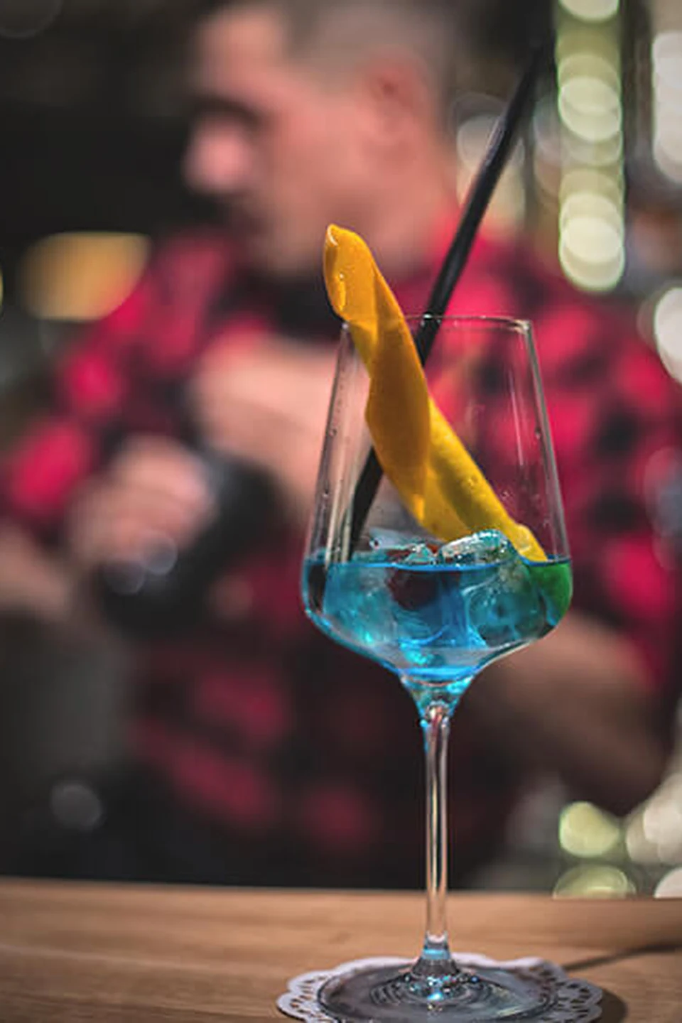 Blauer Cocktail mit Mangoscheibe und schwarzem Strohhalm im Weinglas auf der Bar des Restaurants Gaspis Gerlos.