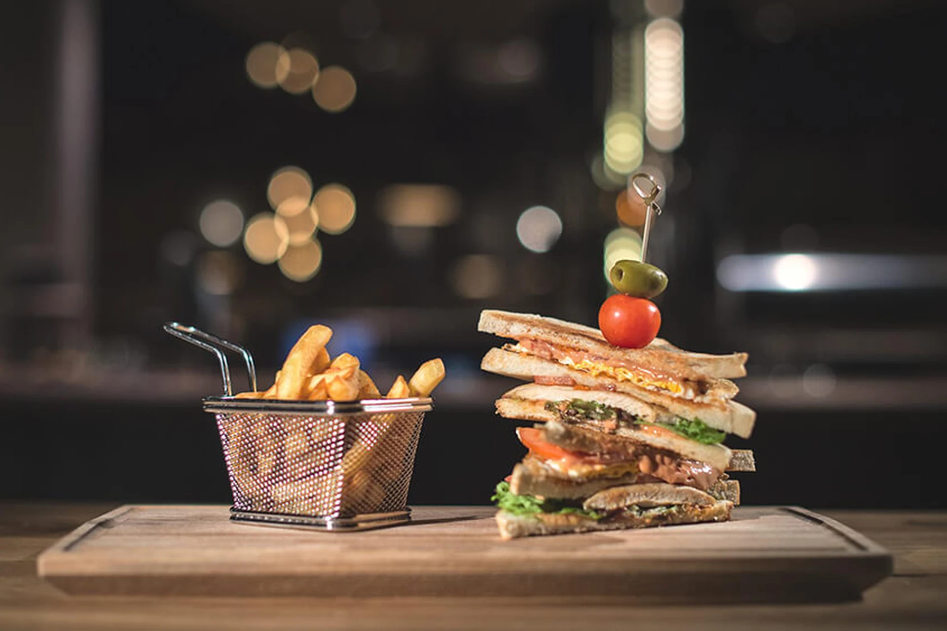 Mehrstöckiges Club Sandwich mit Pommes frites im Metallkörbchen auf einem Holzbrett im Restaurant Gaspis Gerlos.