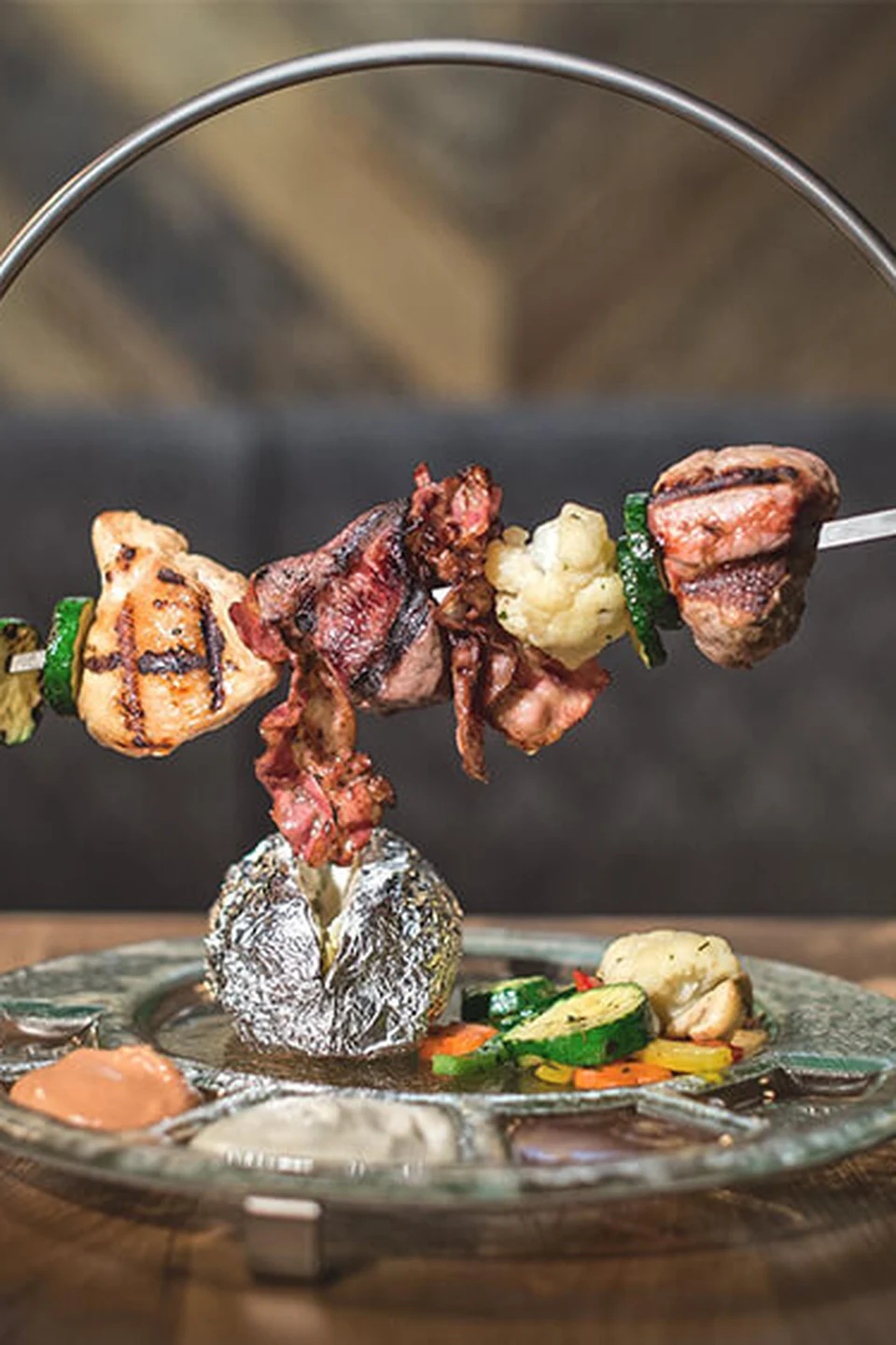 Gegrillter Fleischspieß mit Gemüse und Folienkartoffel auf einem runden Teller im Restaurant Gaspis Gerlos.