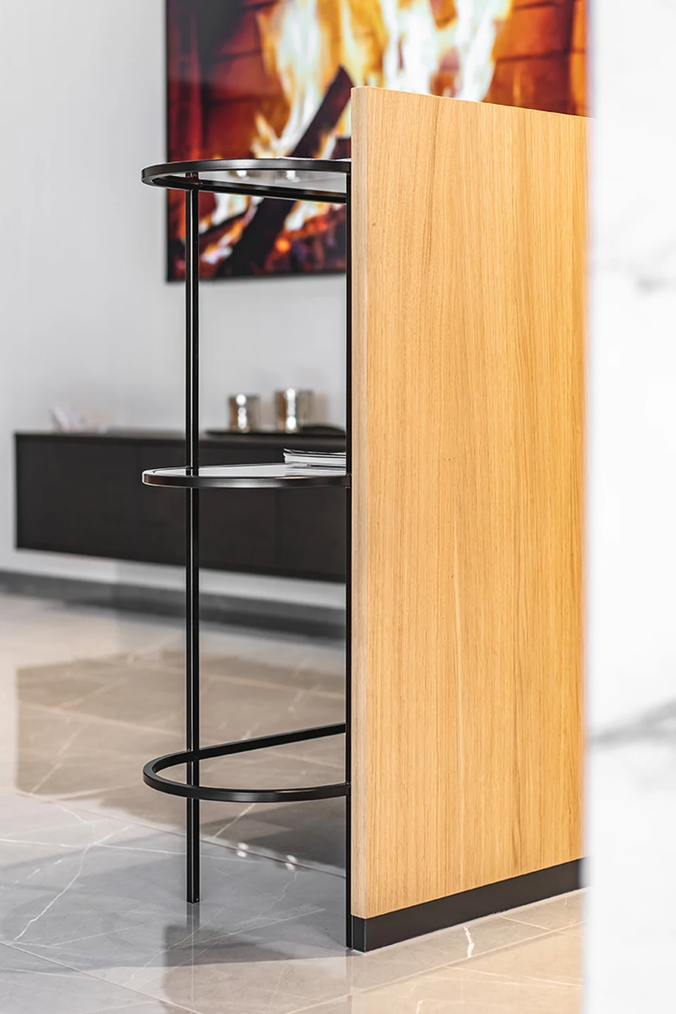 Detailansicht eines schwarzen Metallregals neben einer Holzlamelle im RE/MAX Immowest Büro Feldkirch mit Marmorboden und Kaminbild im Hintergrund.