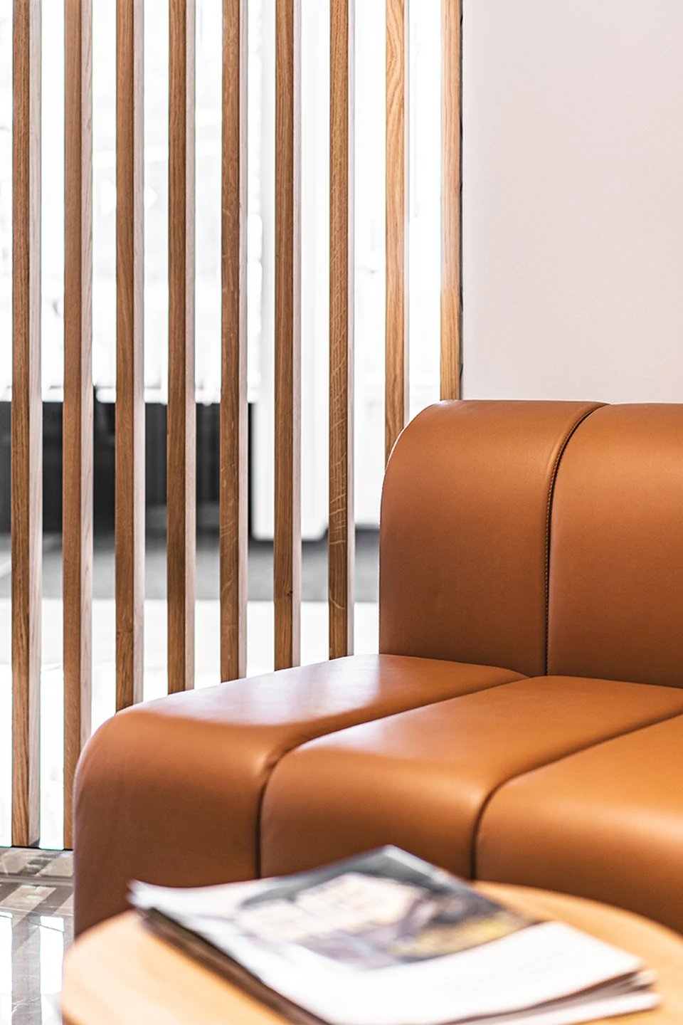 Detailansicht eines cognacfarbenen Ledersofas mit Holzlamellentrennwand im Wartebereich des RE/MAX Immowest Büros Feldkirch.