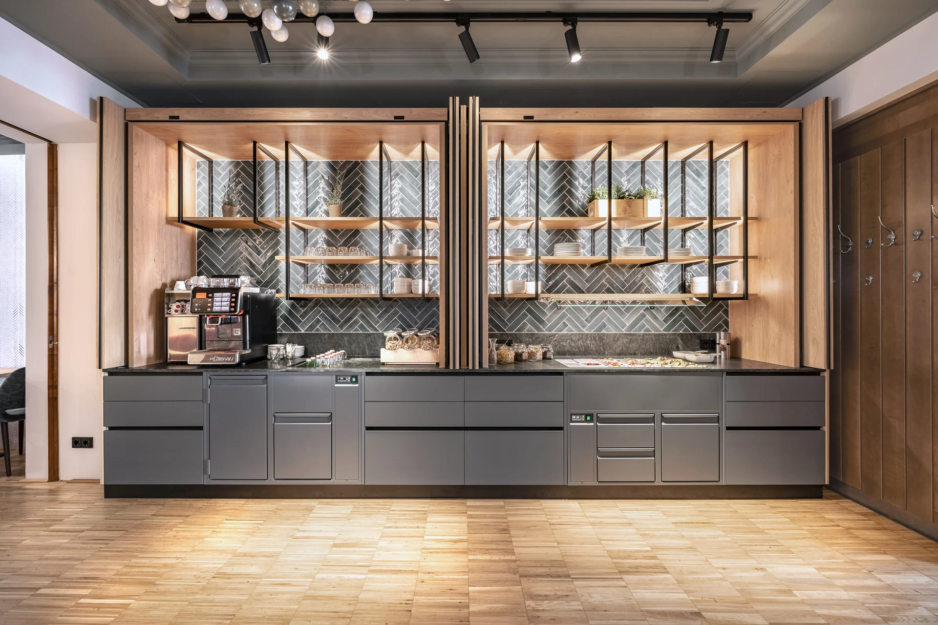 Buffet- und Kaffeestation im Restaurant des Hotel-Gasthof Graf St. Pölten mit grauer Küchenzeile, offenen Holzregalen, Fischgrät-Wandfliesen in Grau und einer Kaffeemaschine vor hellem Holzparkett.