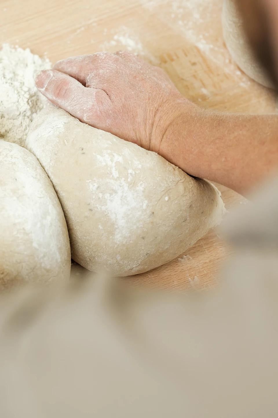 Detailaufnahme eines Bäckers beim Kneten von Brotteig auf einer bemehlten Holzarbeitsplatte in der Bäckerei im Gwölb.