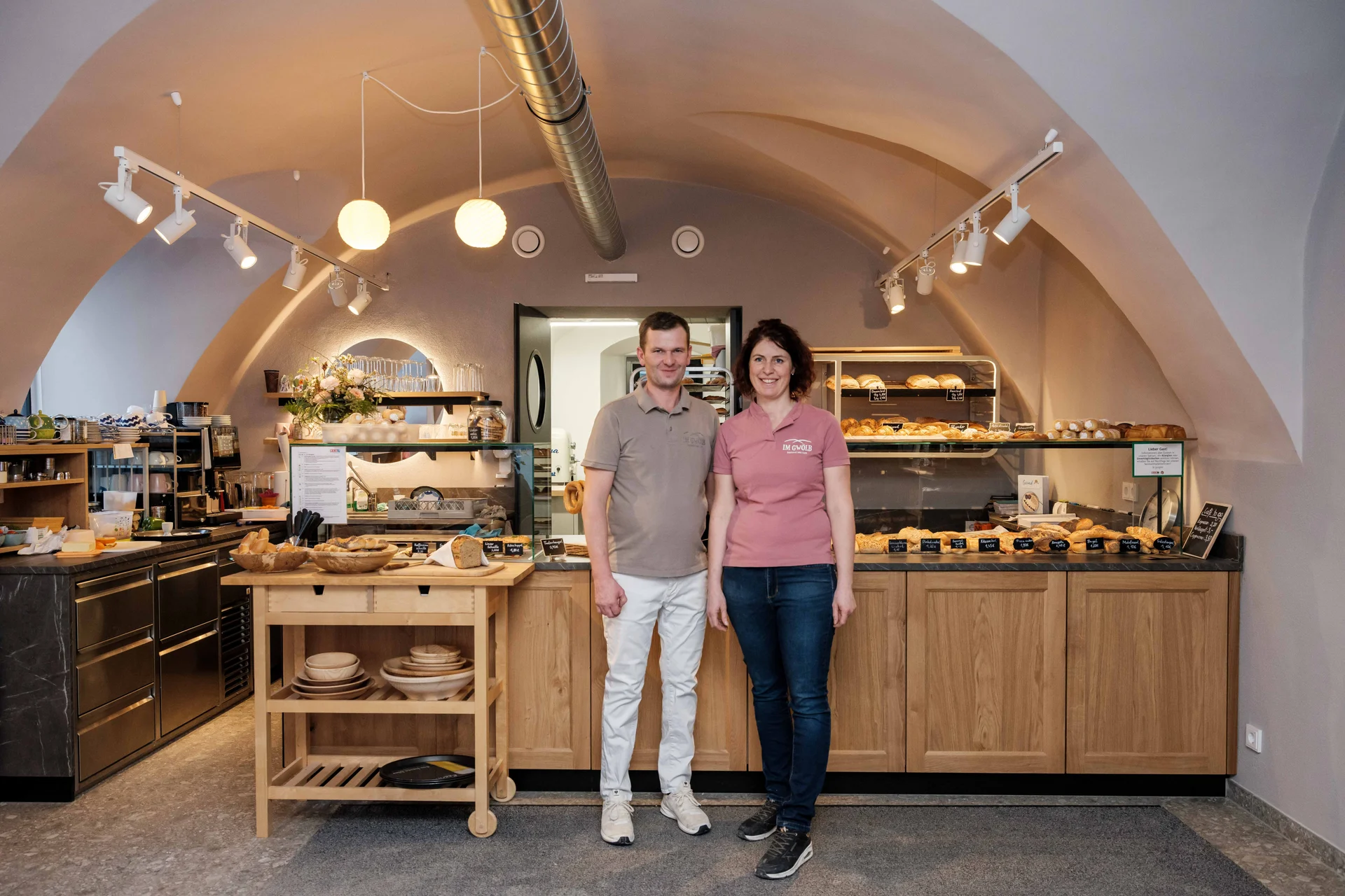 Inhaberpaar der Bäckerei im Gwölb vor der Verkaufstheke mit frischem Gebäck unter einem historischen Gewölbebogen.