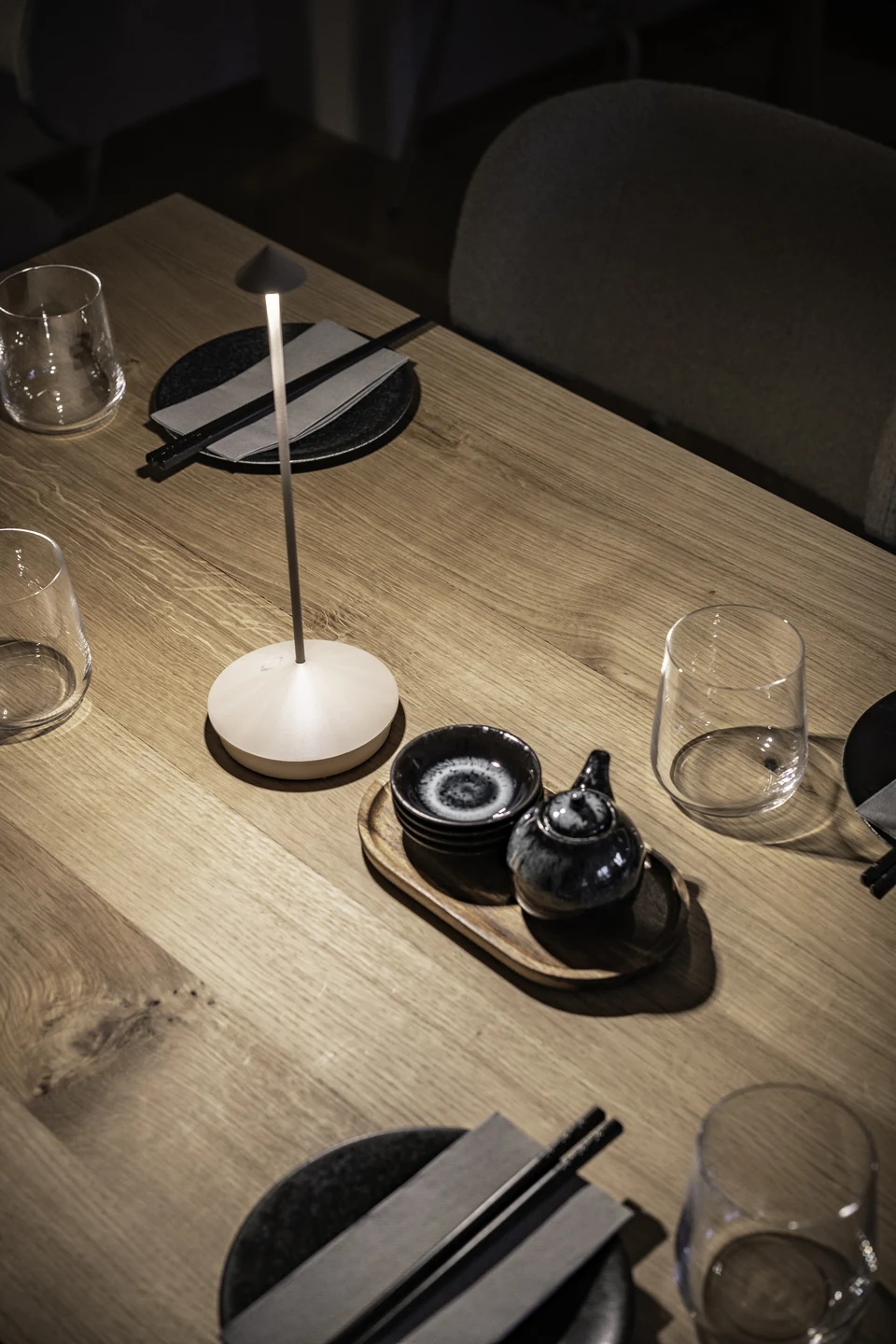 Detail des Tischgedeck im Hanako Dornbirn mit Tischlampe, schwarzem Keramikgeschirr, Stäbchen und Glaswaren auf Holztisch.