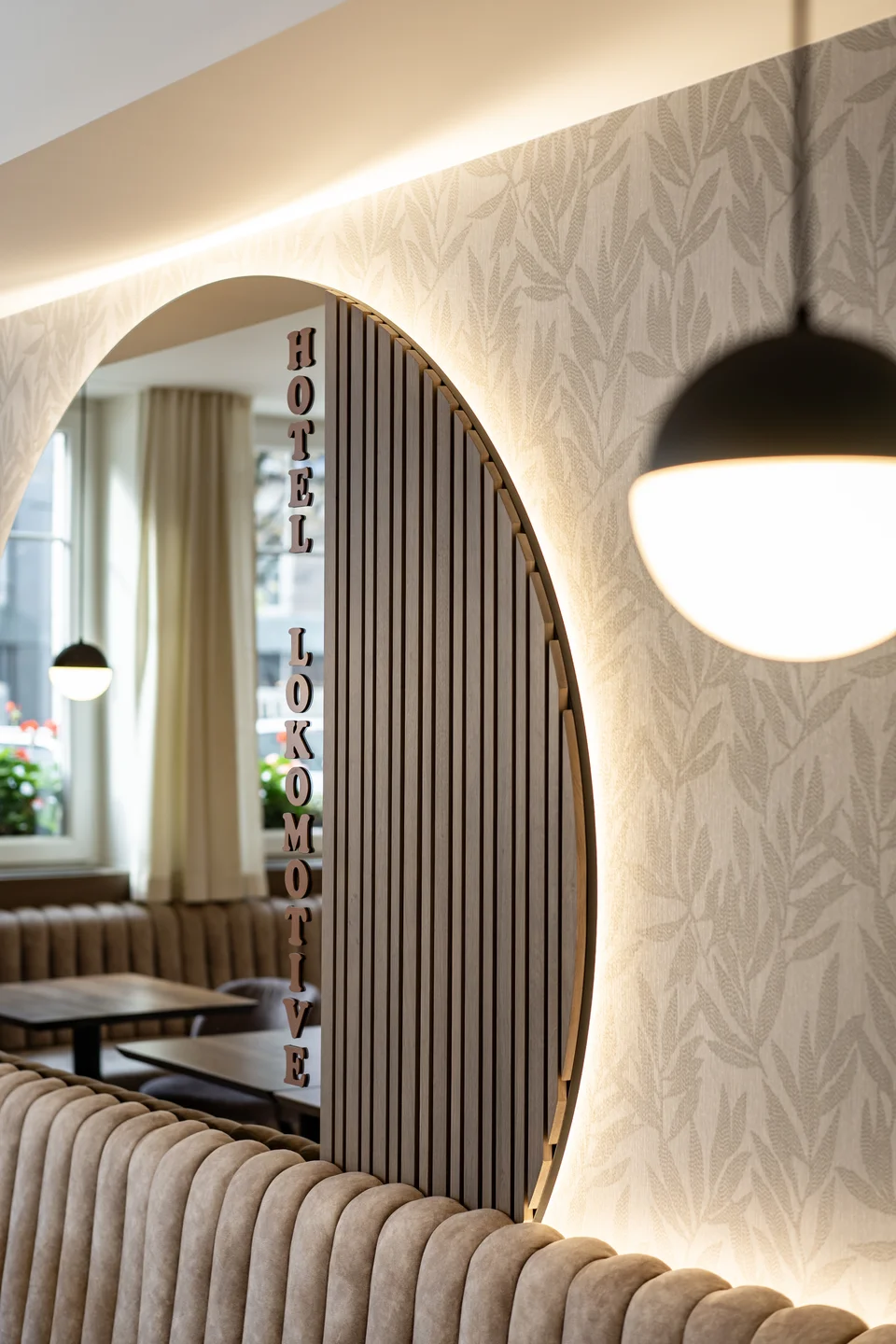 Designelement im Hotel Lokomotive Linz mit rundem Holzlamellen-Raumteiler mit vertikalem Schriftzug „Hotel Lokomotive