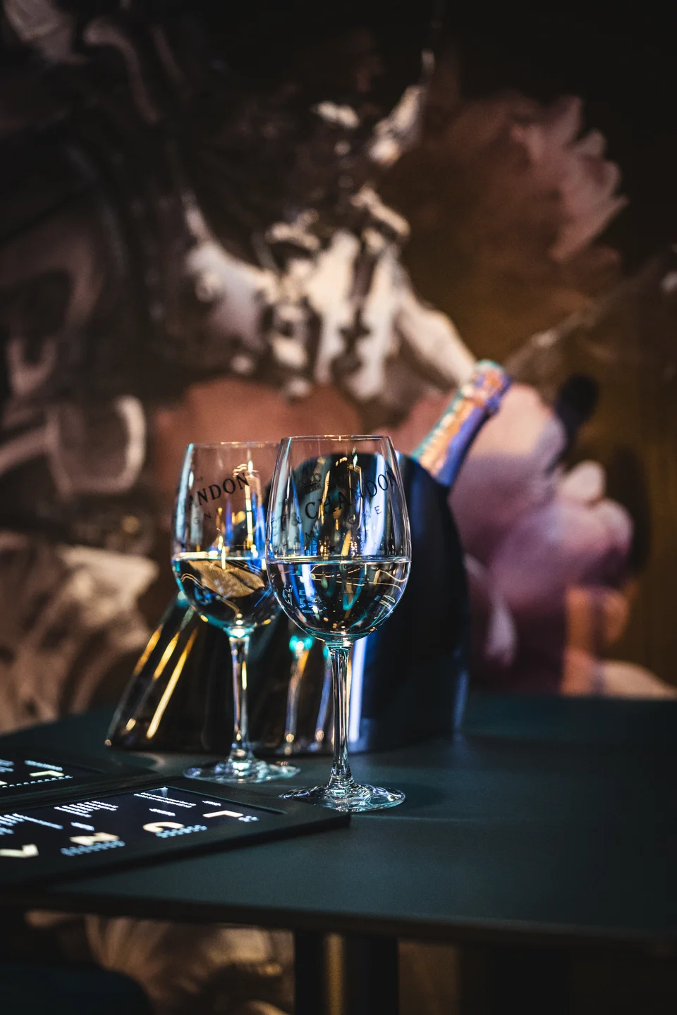 Detailaufnahme im Club Luna Innsbruck mit zwei Chandon-Weingläsern auf einem dunklen Tisch vor abstraktem LED-Screen-Hintergrund in Blau- und Lilatönen.